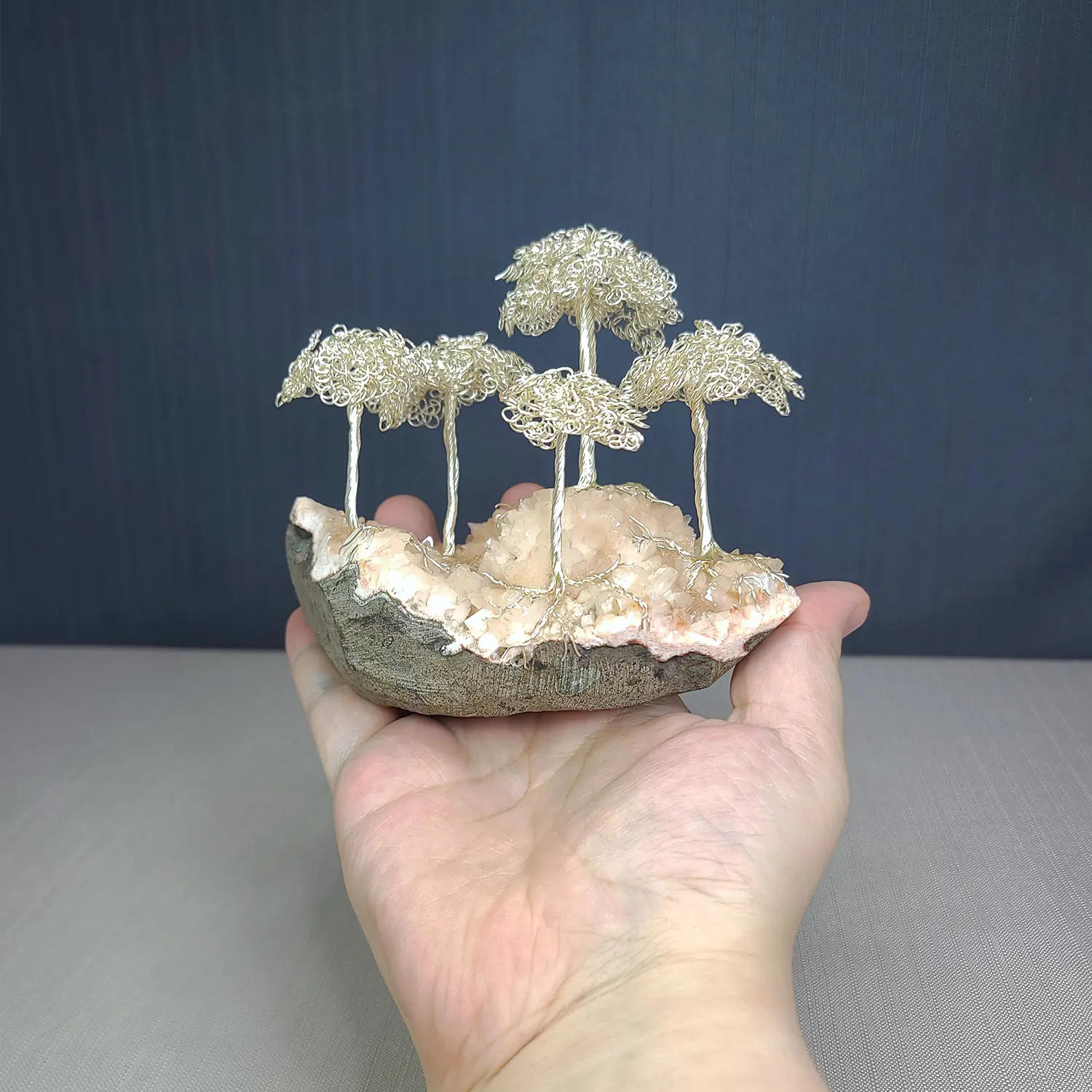 Hand holding a small sculpture of wire trees on a rock against a dark background