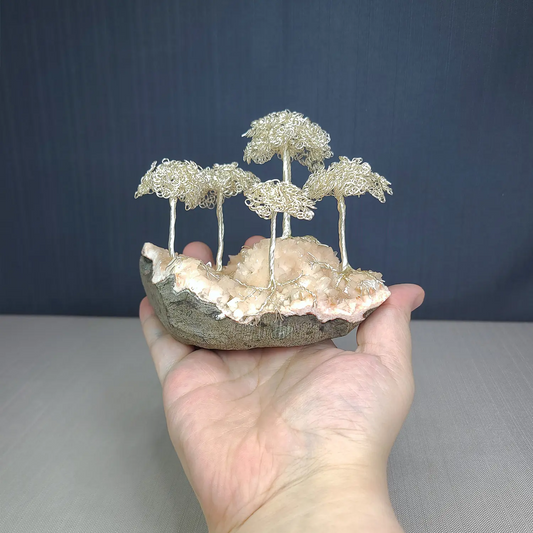 Hand holding a small sculpture of wire trees on a rock against a dark background