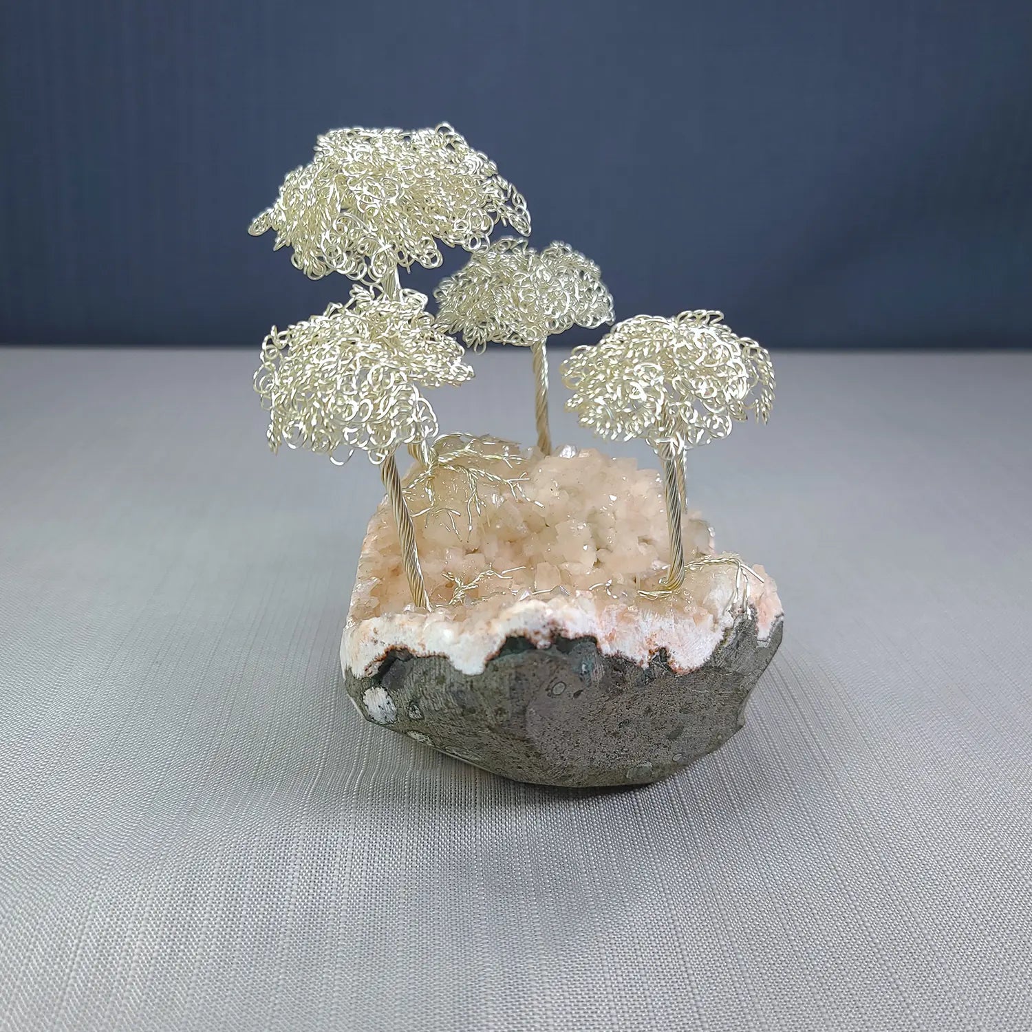 Decorative piece with wire trees on a stone base against a blue background