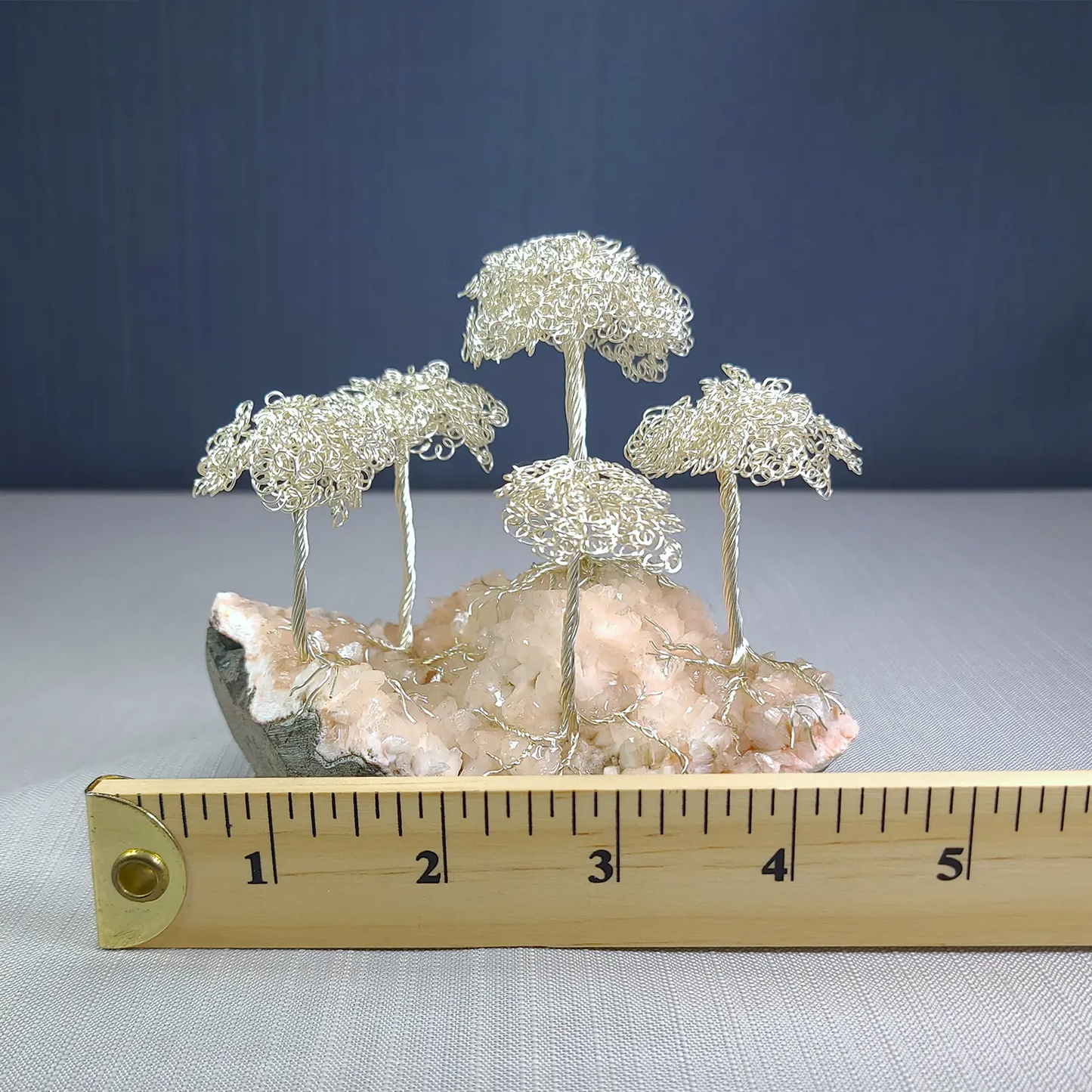 Wire tree sculpture on a rock with a ruler for scale against a blue background