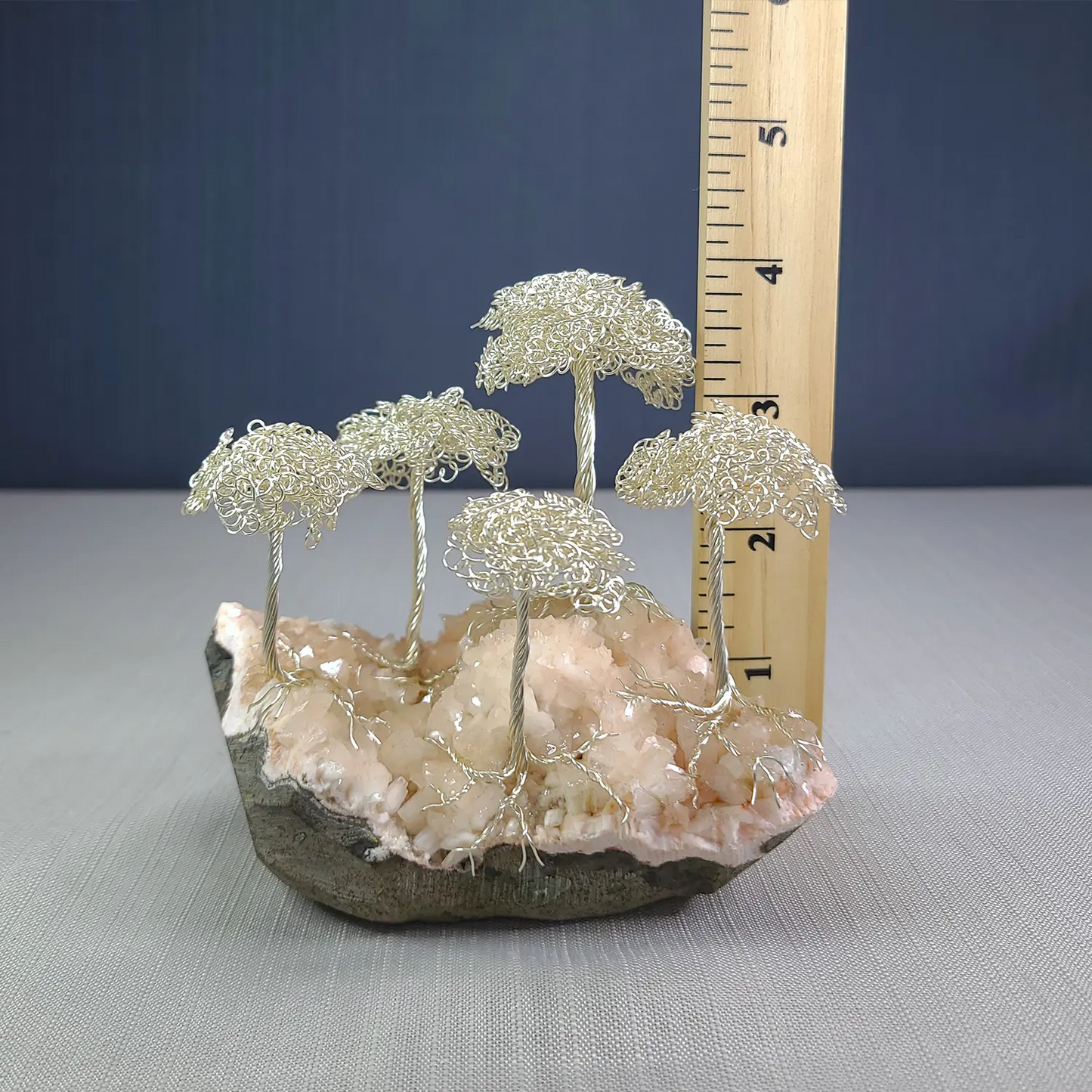 Decorative arrangement of wire trees on a rock with a ruler for scale against a blue background