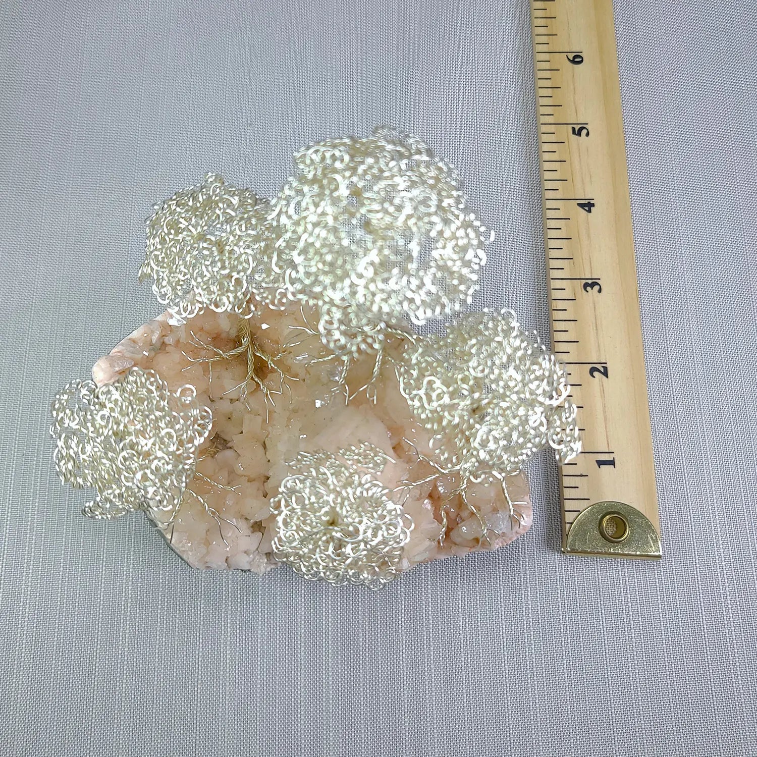 Decorative metal flower clusters on a stone base with a ruler for scale on a gray background