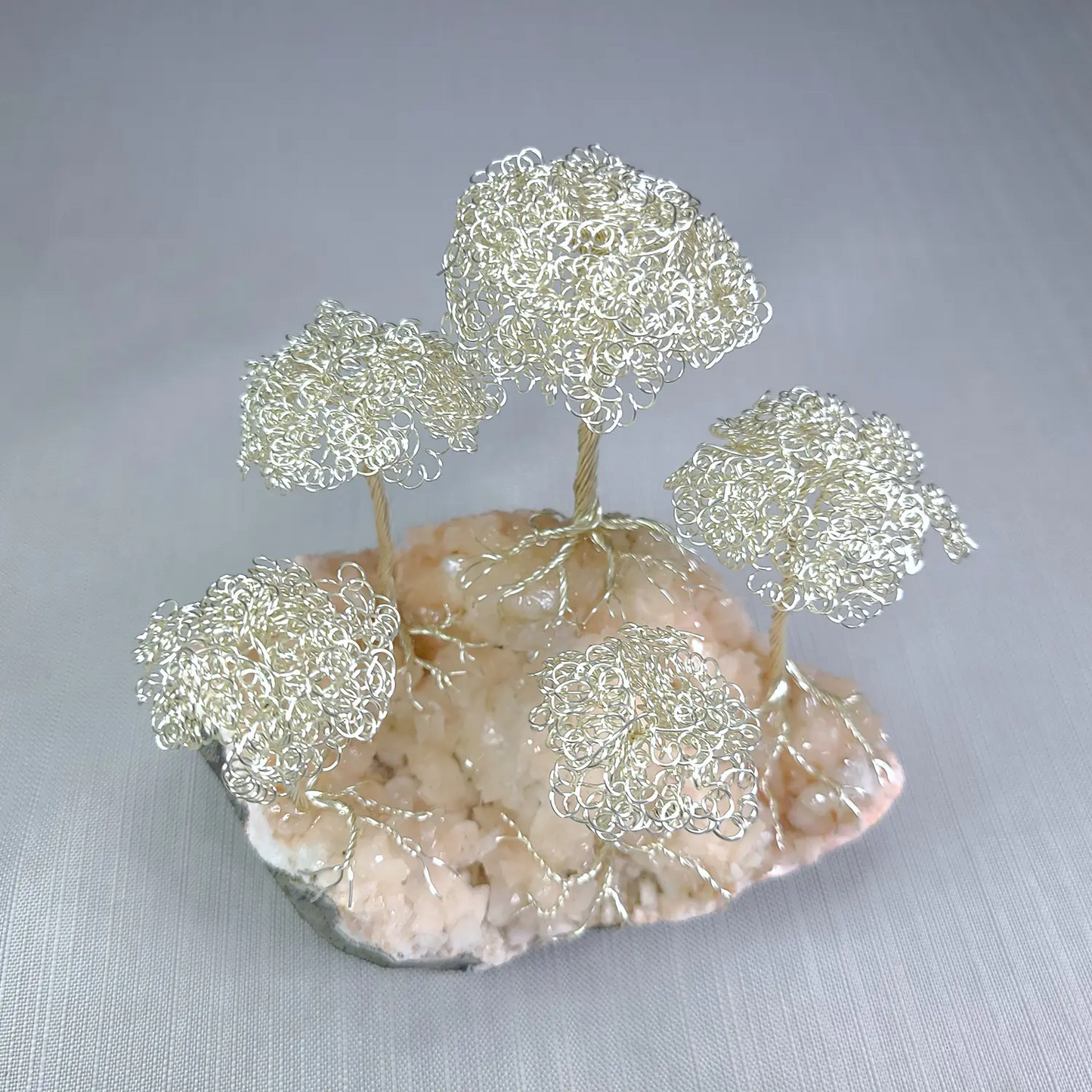 Decorative wire tree sculpture on a stone base with a gray background