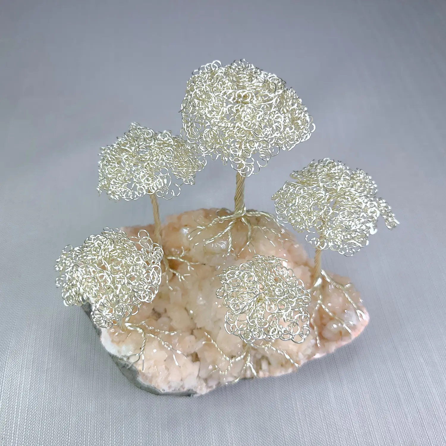 Decorative wire tree sculpture on a stone base with a gray background