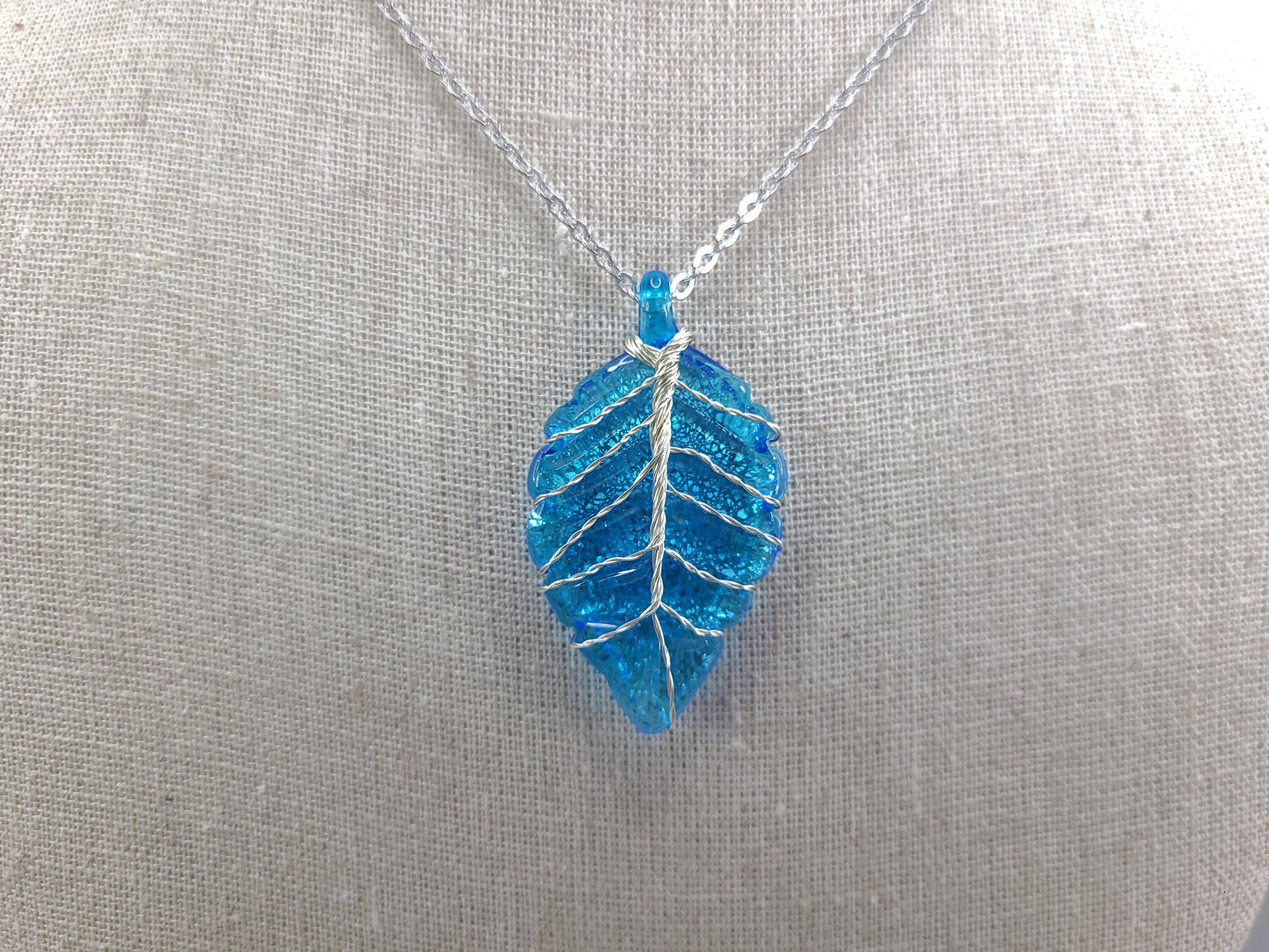 Blue leaf-shaped pendant on a silver chain against a gray background