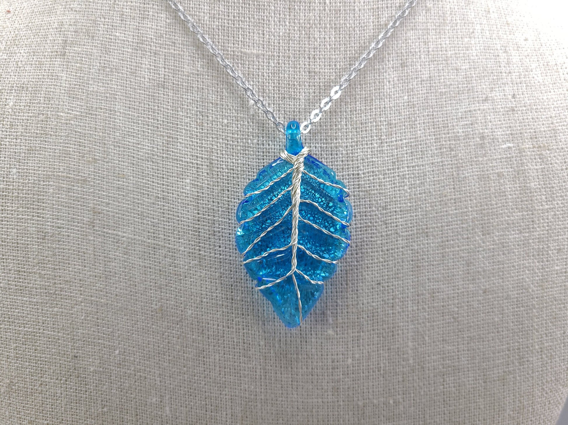 Blue leaf-shaped pendant on a silver chain against a gray background