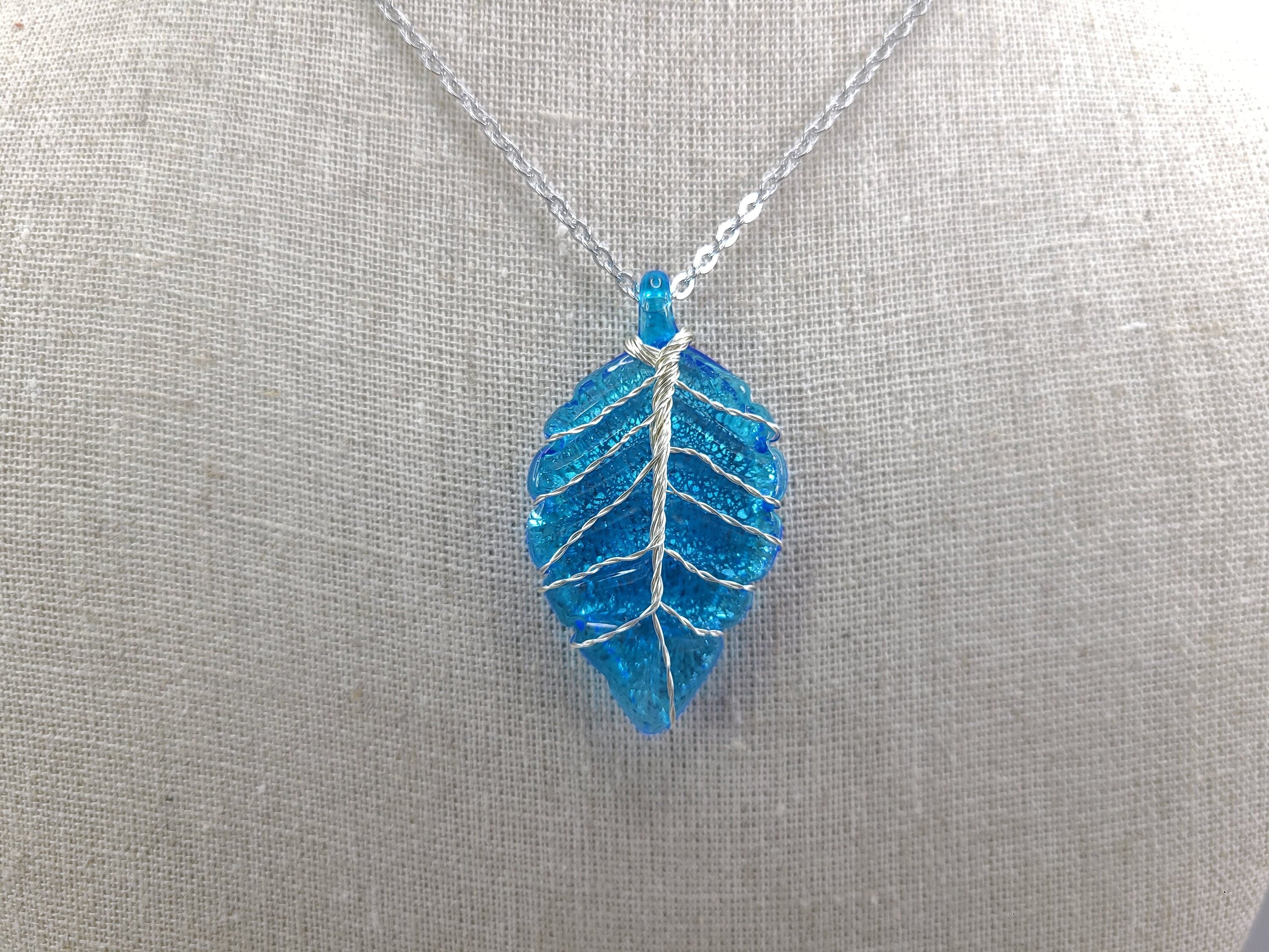 Blue leaf-shaped pendant on a silver chain against a gray background