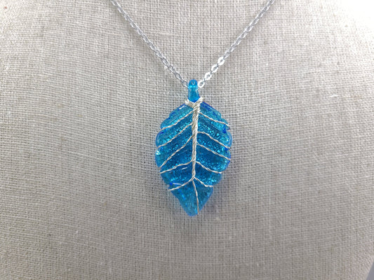 Blue leaf-shaped pendant on a silver chain against a gray background