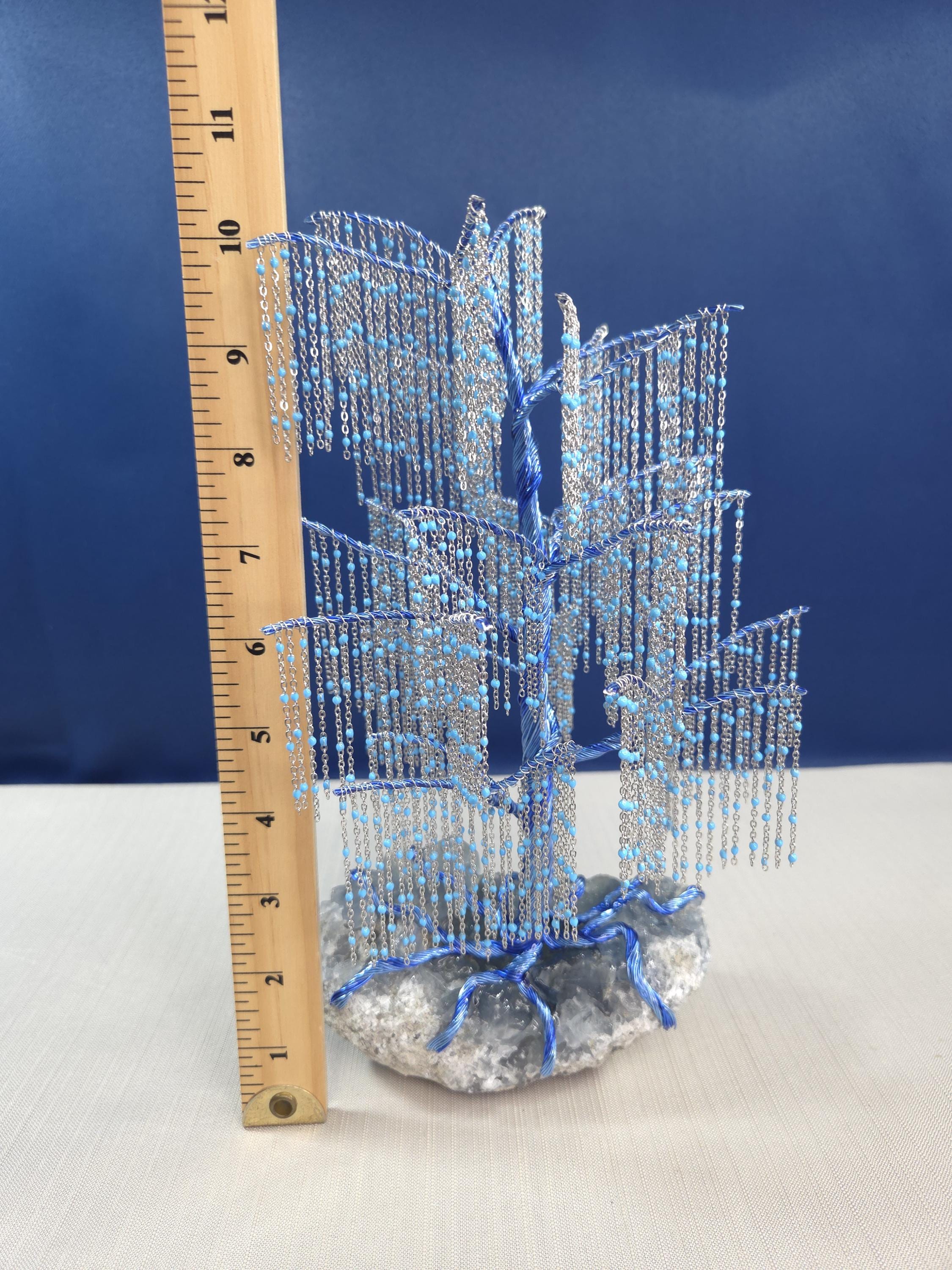Decorative blue and silver tree sculpture with a ruler for scale on a white surface.