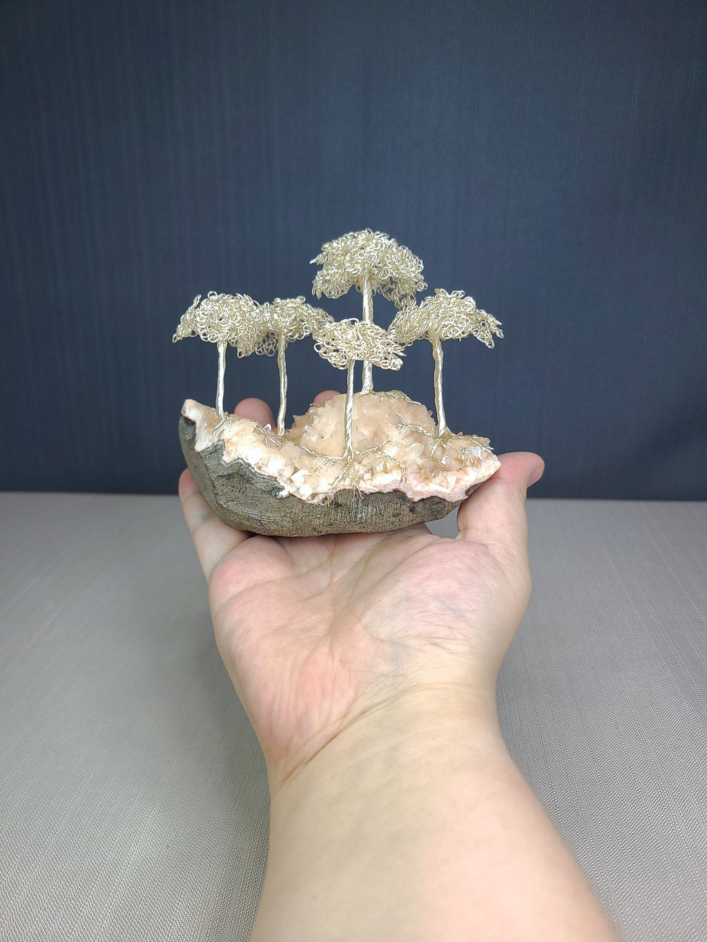 Hand holding a small sculpture of wire trees on a rock against a dark blue background