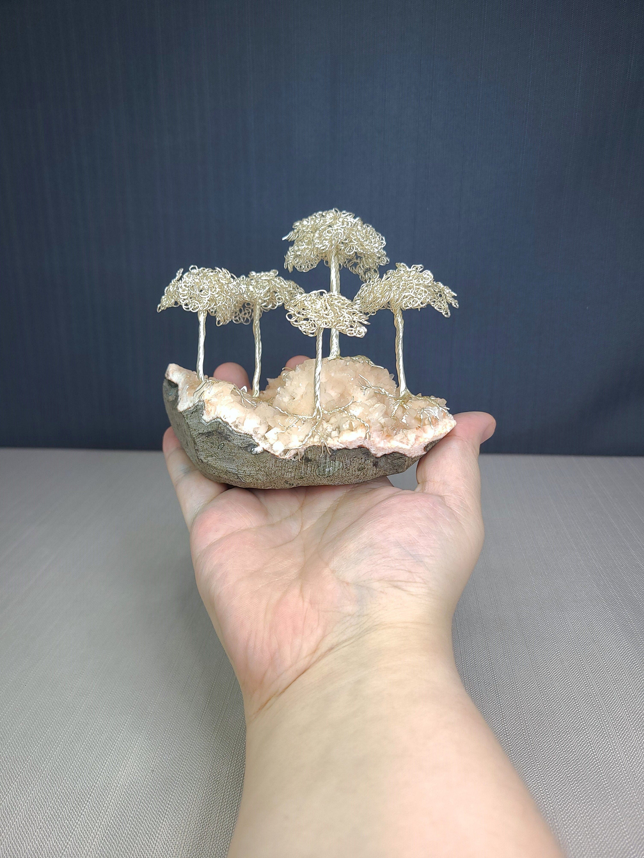 Hand holding a small sculpture of wire trees on a rock against a dark blue background