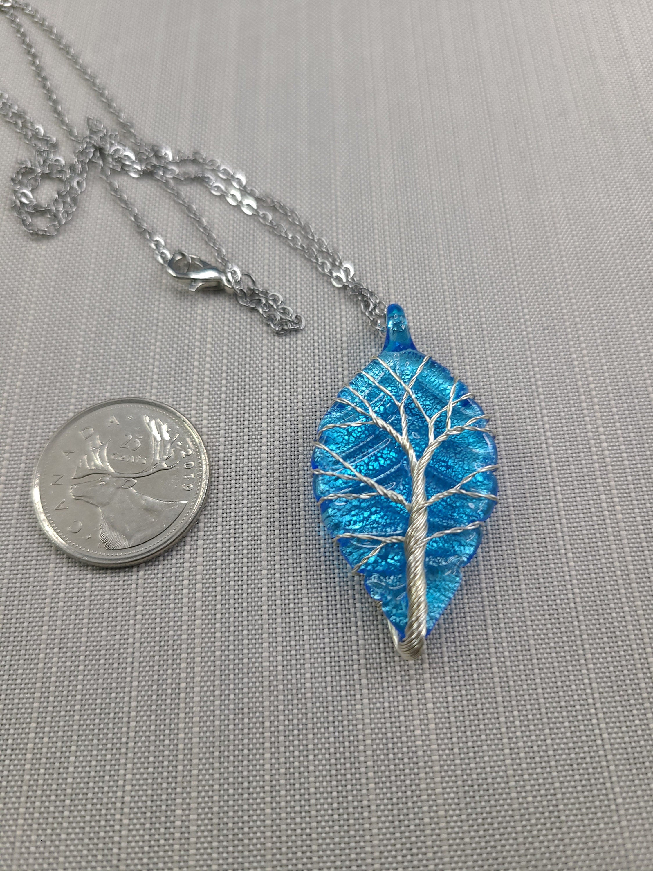 Blue leaf-shaped pendant with silver tree design on a gray background