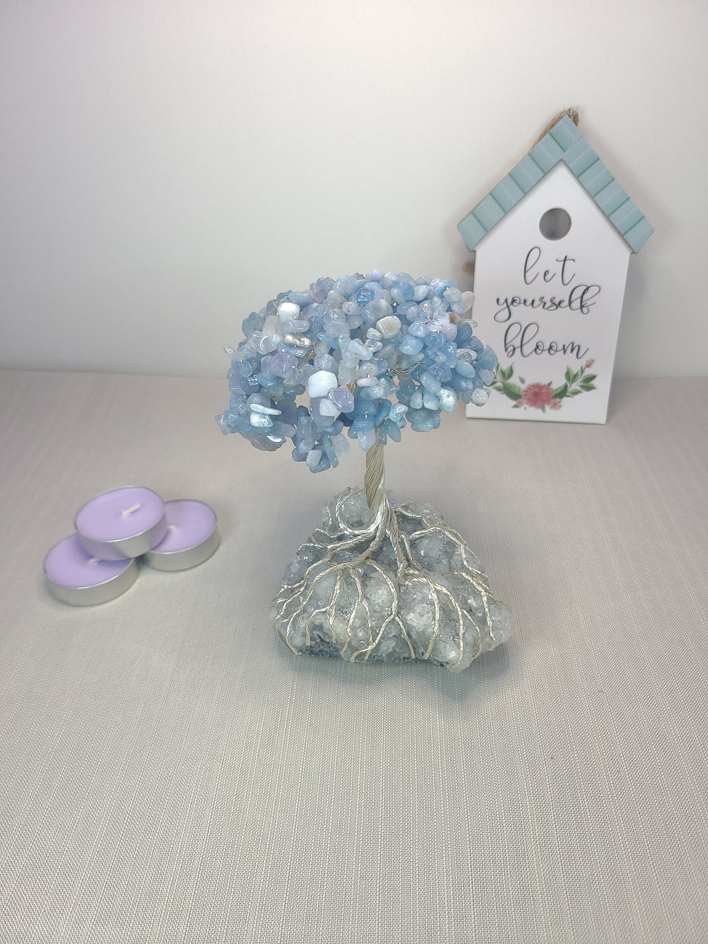 Decorative blue crystal tree with candles and a sign on a light gray surface