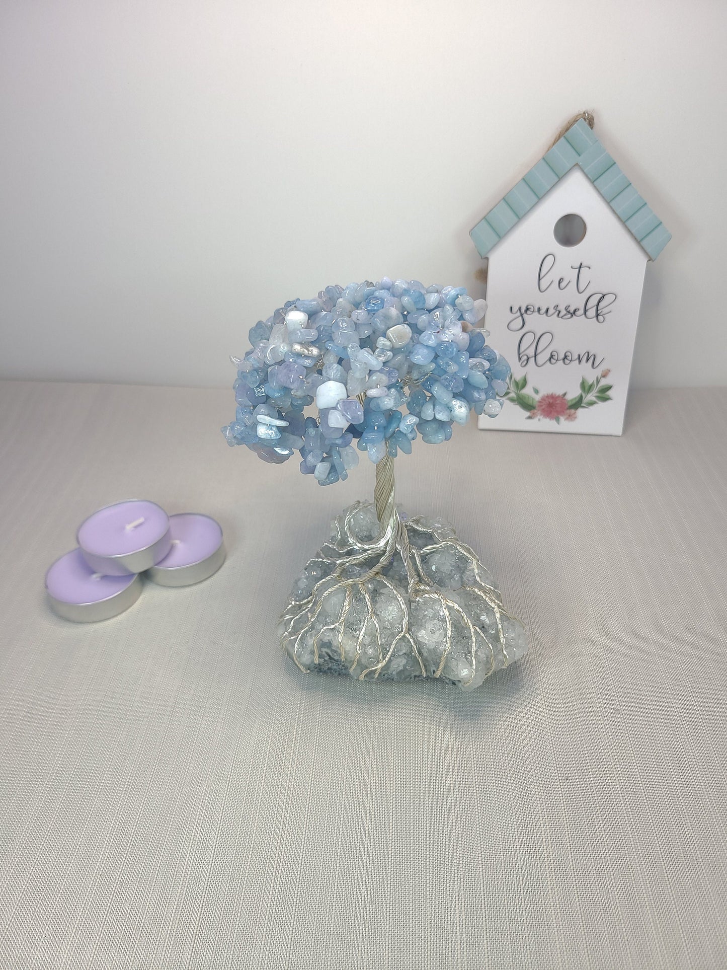 Decorative blue crystal tree with candles and a sign on a light gray surface