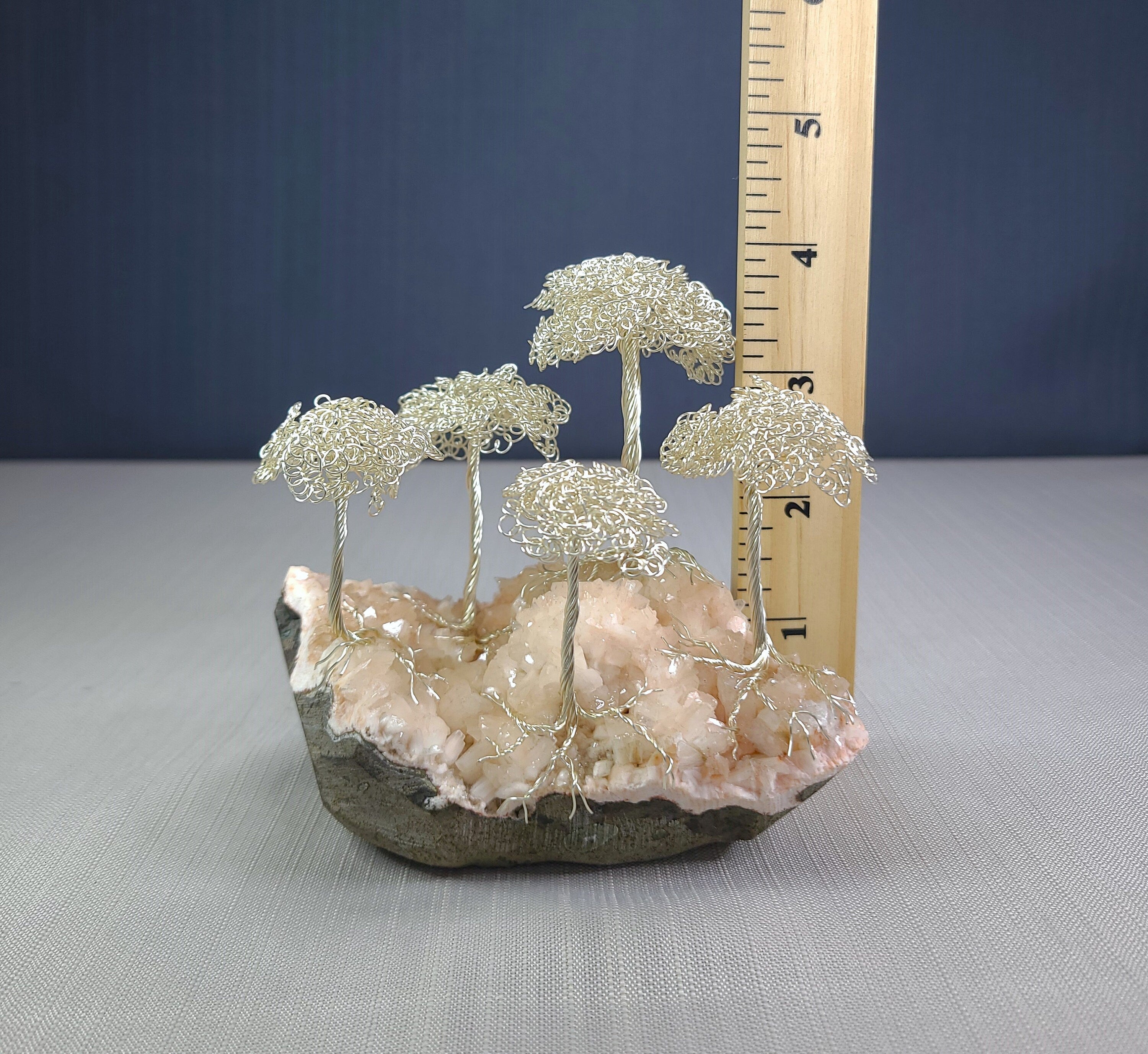 Decorative arrangement of wire trees on a rock with a ruler for scale against a blue background