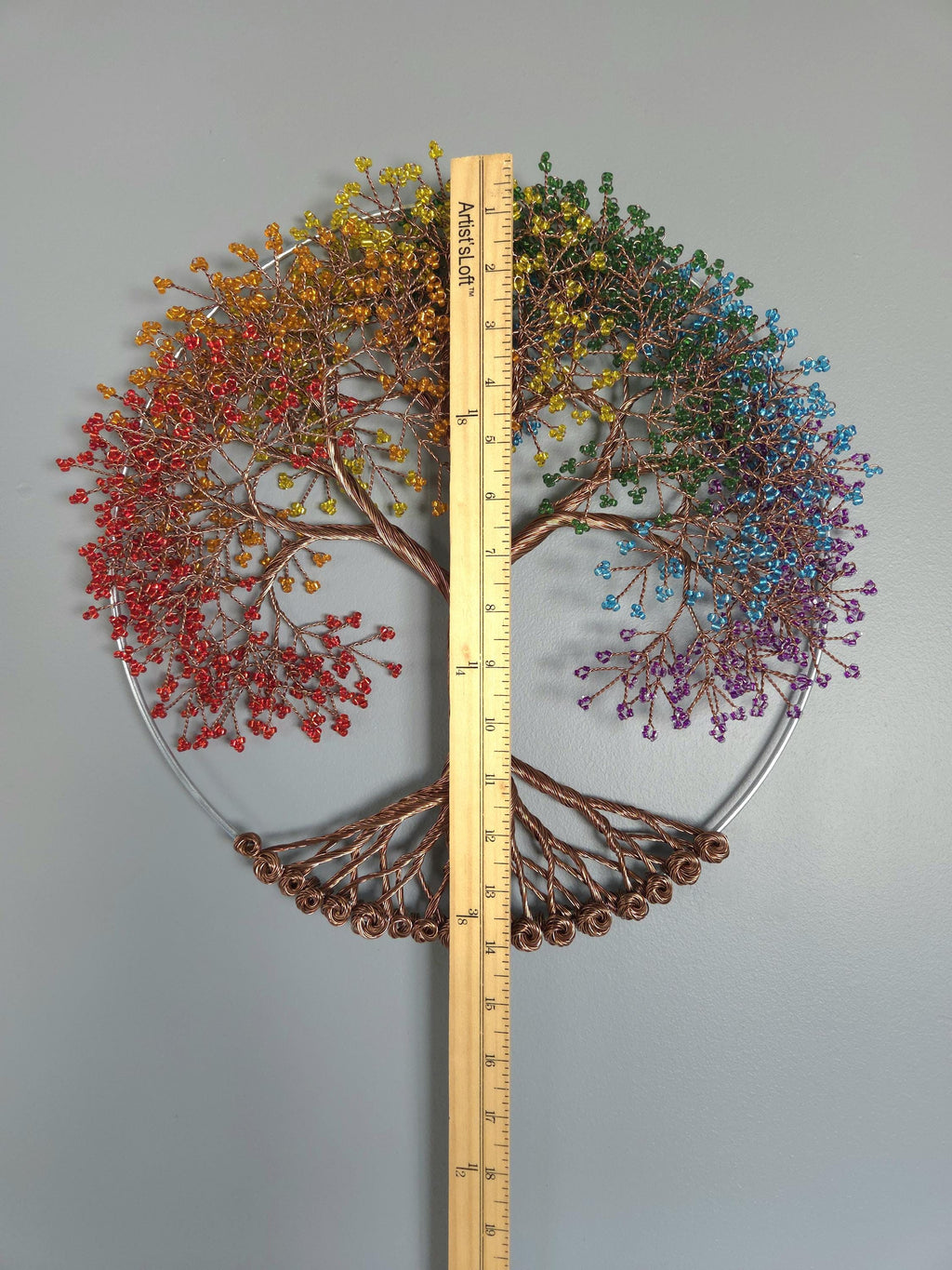 Decorative wall art with a tree design made of colorful beads, accompanied by a ruler for scale.