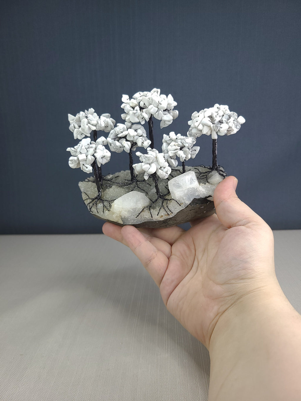 Hand holding a small sculpture of white flowers on a gray surface with a dark blue background