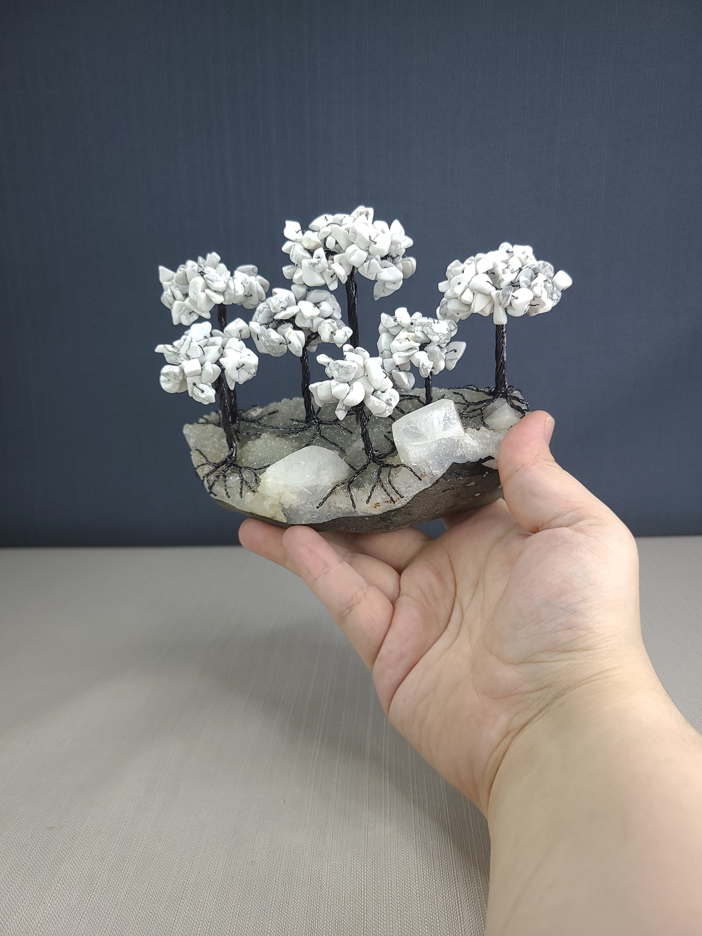 Hand holding a small sculpture of white flowers on a gray surface with a dark blue background
