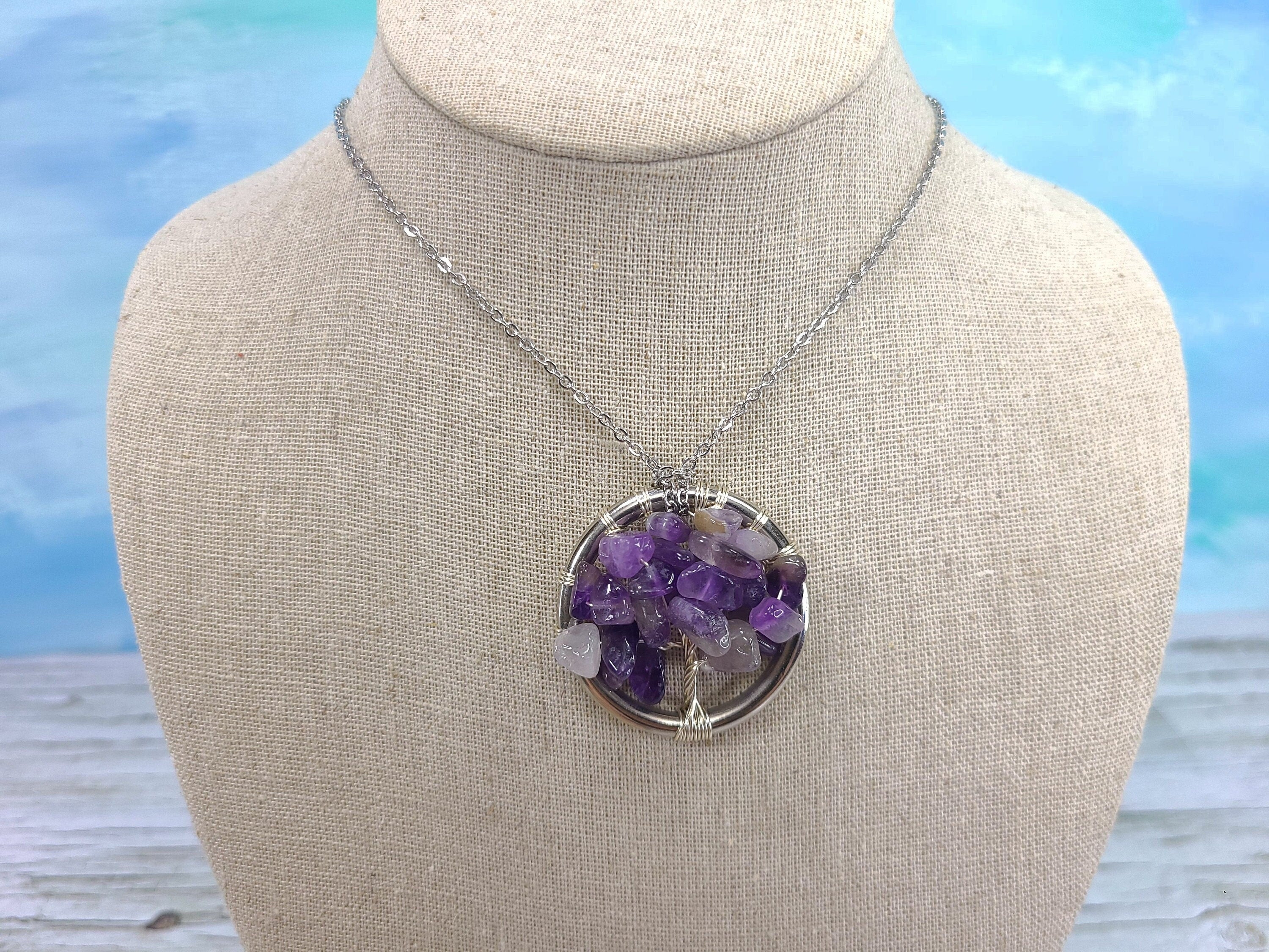 Necklace with a round pendant featuring purple and clear stones on a mannequin bust against a blue sky background.
