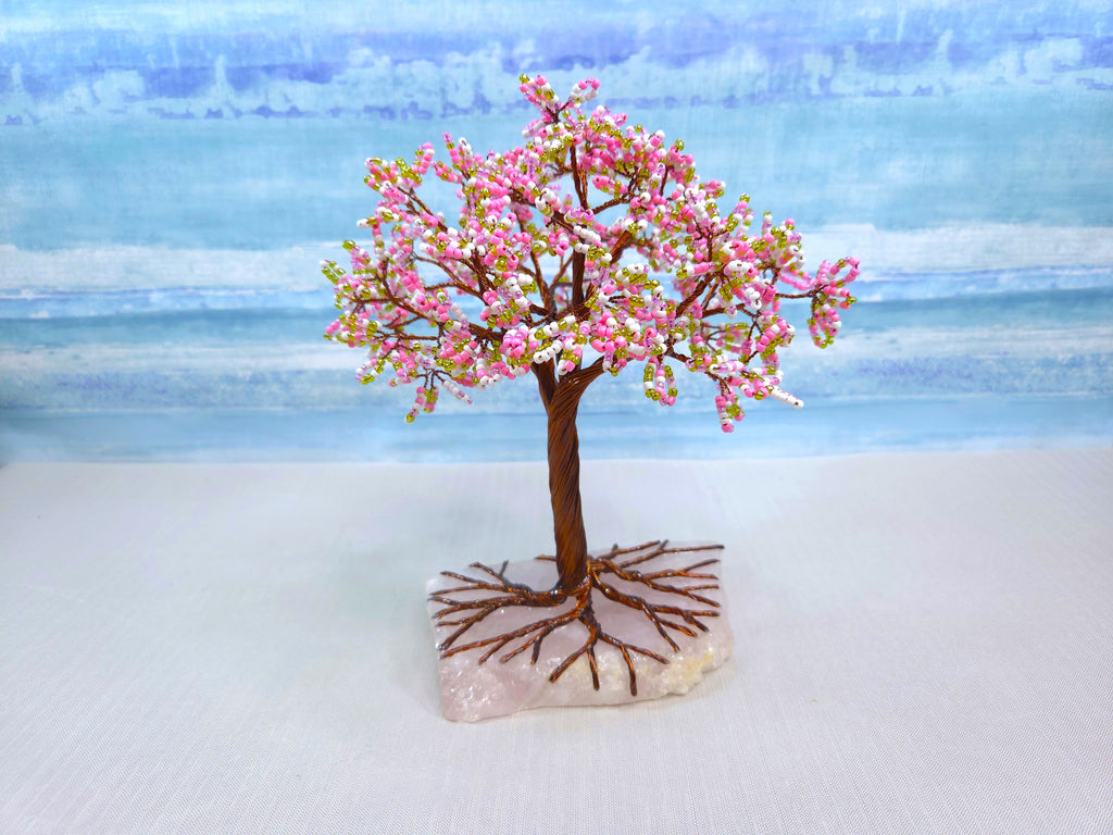 Small decorative tree with pink blossoms on a stone base against a blurred natural background