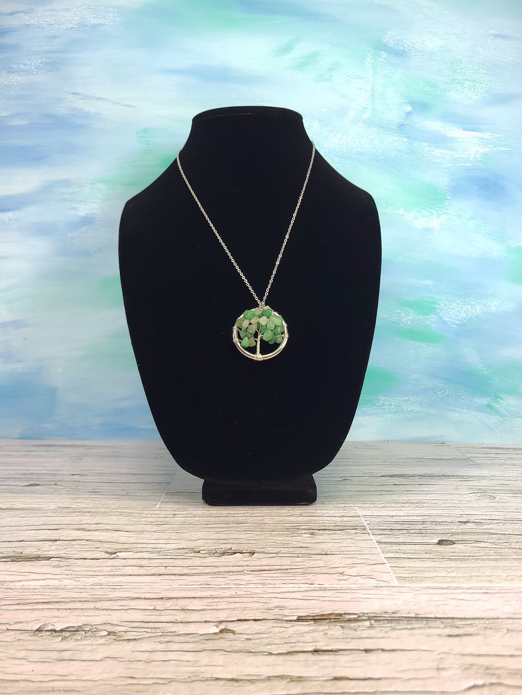 Necklace with a tree of life pendant on a black bust against a blue and green abstract background.