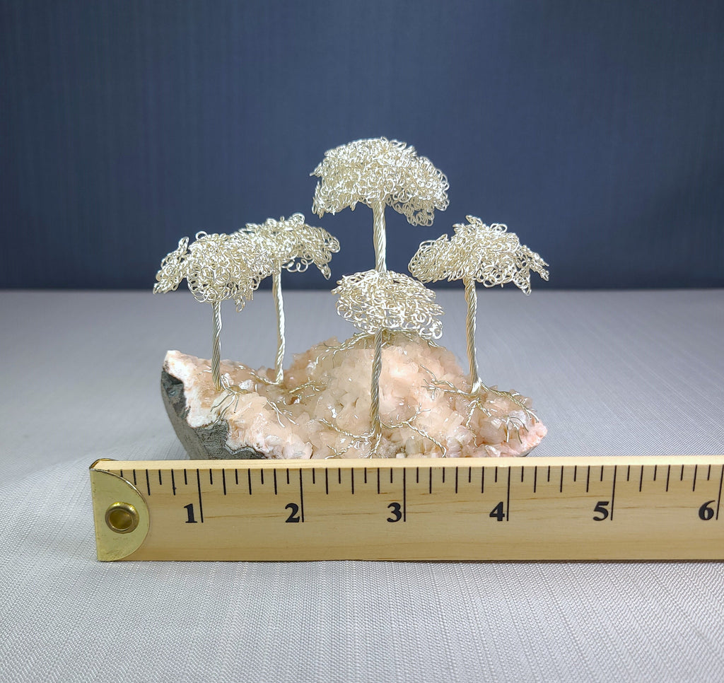 Decorative wire tree sculpture on a rock with a ruler for scale against a blue background