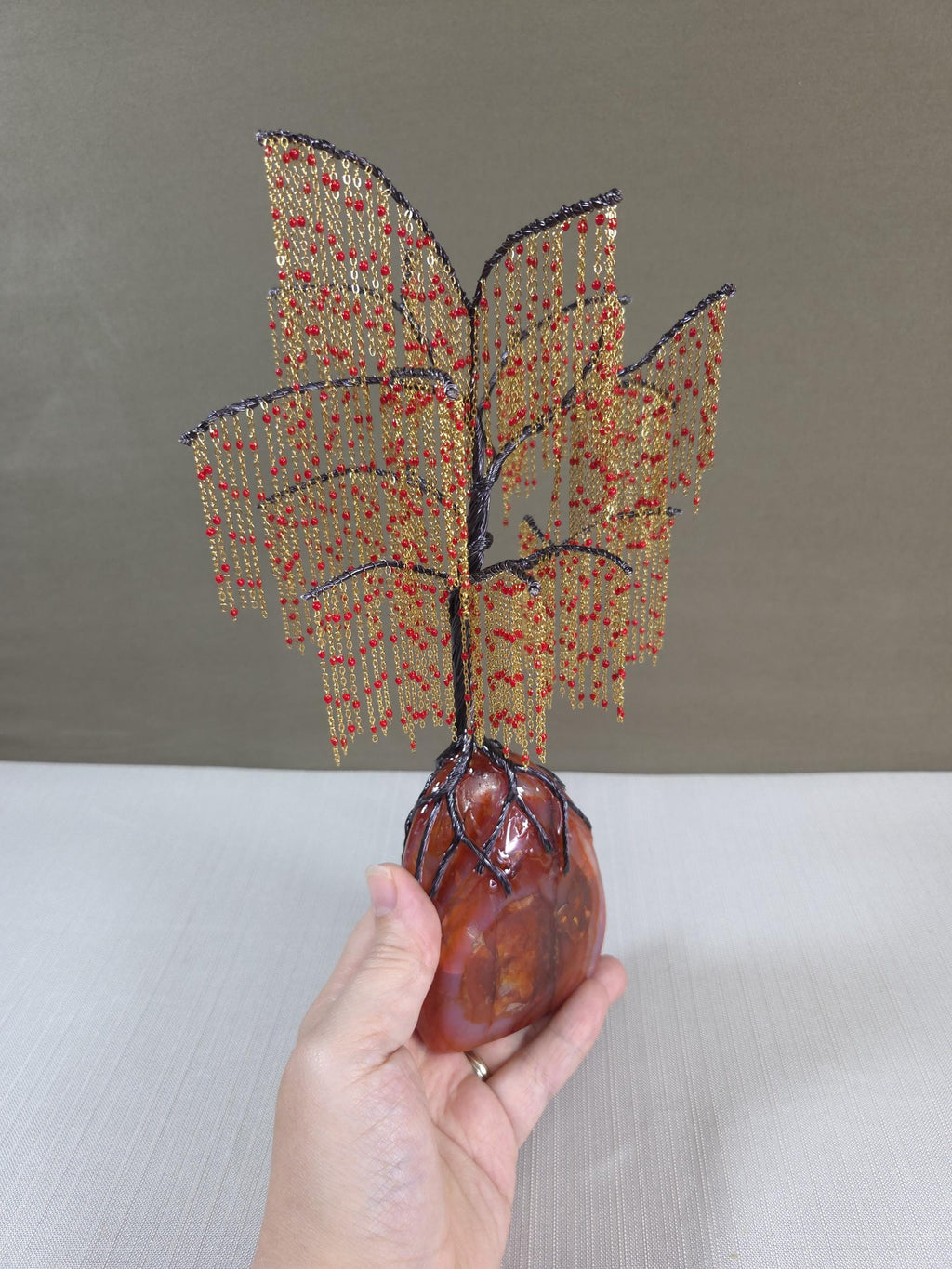 Hand holding a beaded willow sculpture on a neutral background