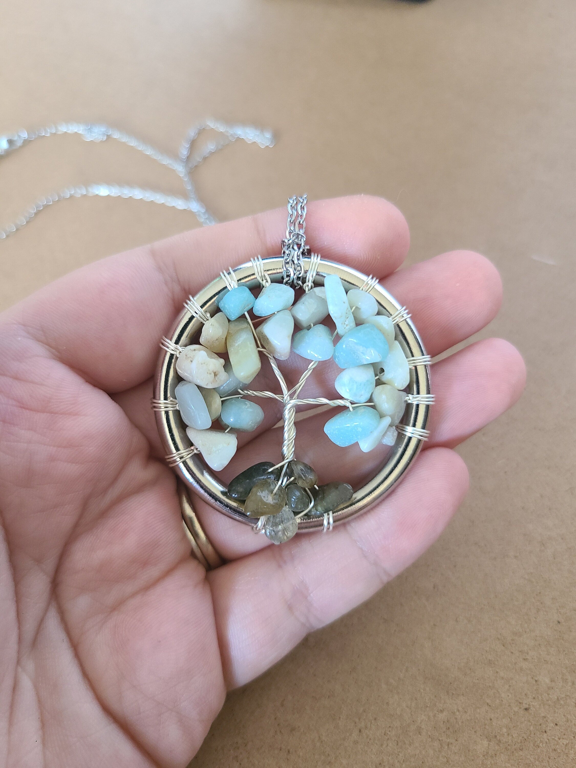 Hand holding a tree of life pendant with stones against a plain background