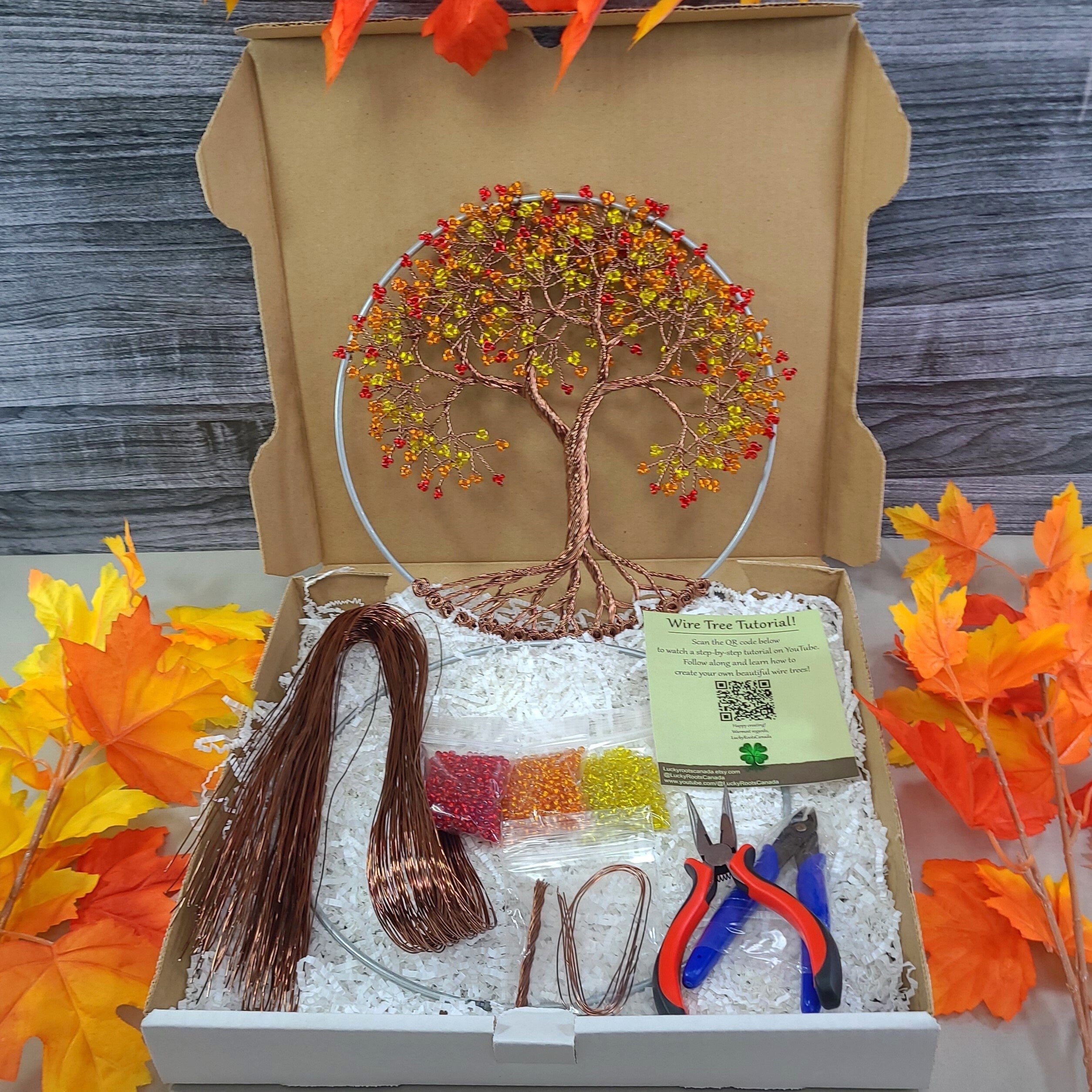 Craft kit with wire tree sculpture, materials, and tools in a box, surrounded by autumn leaves.