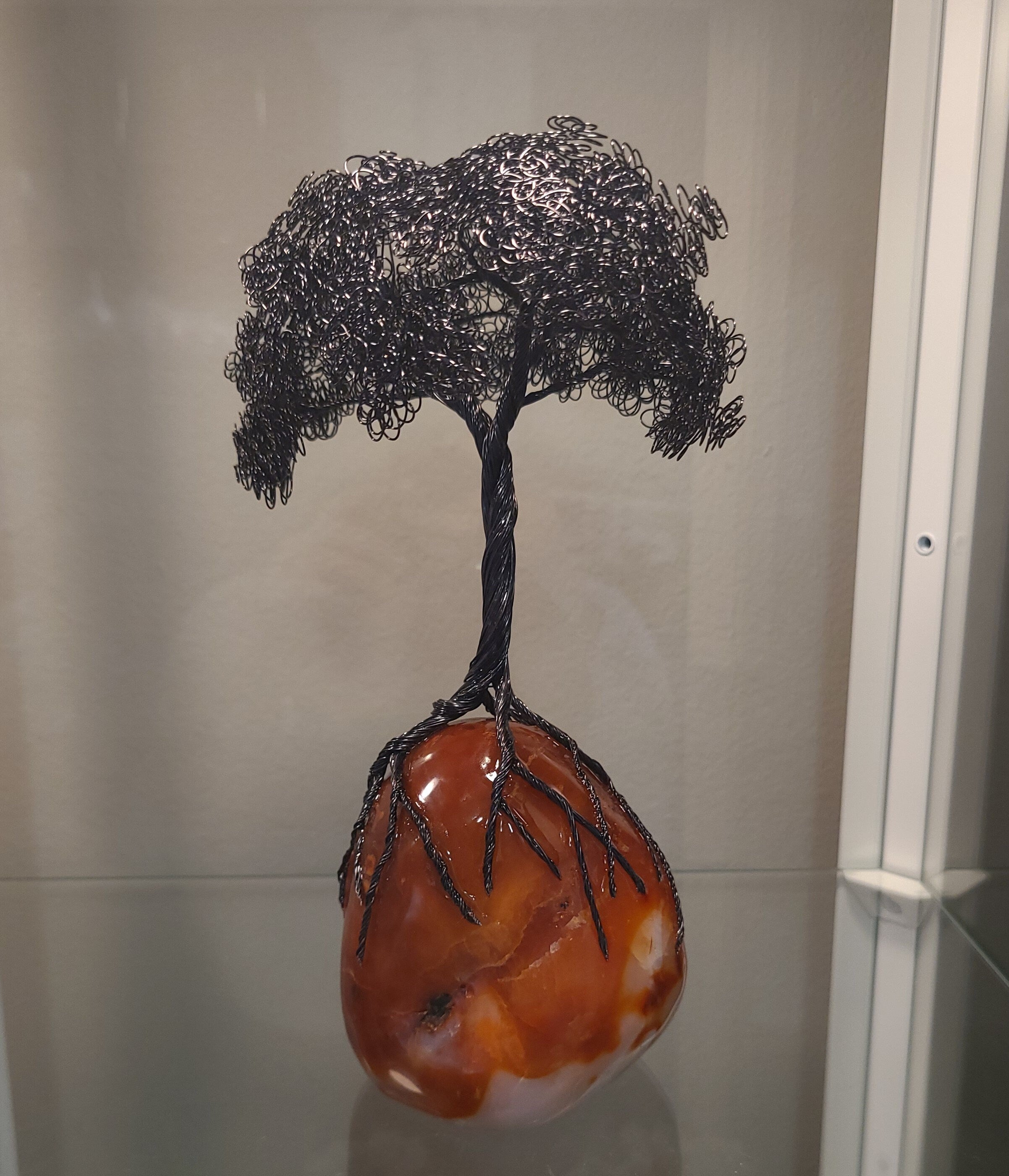 Decorative tree sculpture on an orange stone base against a neutral background