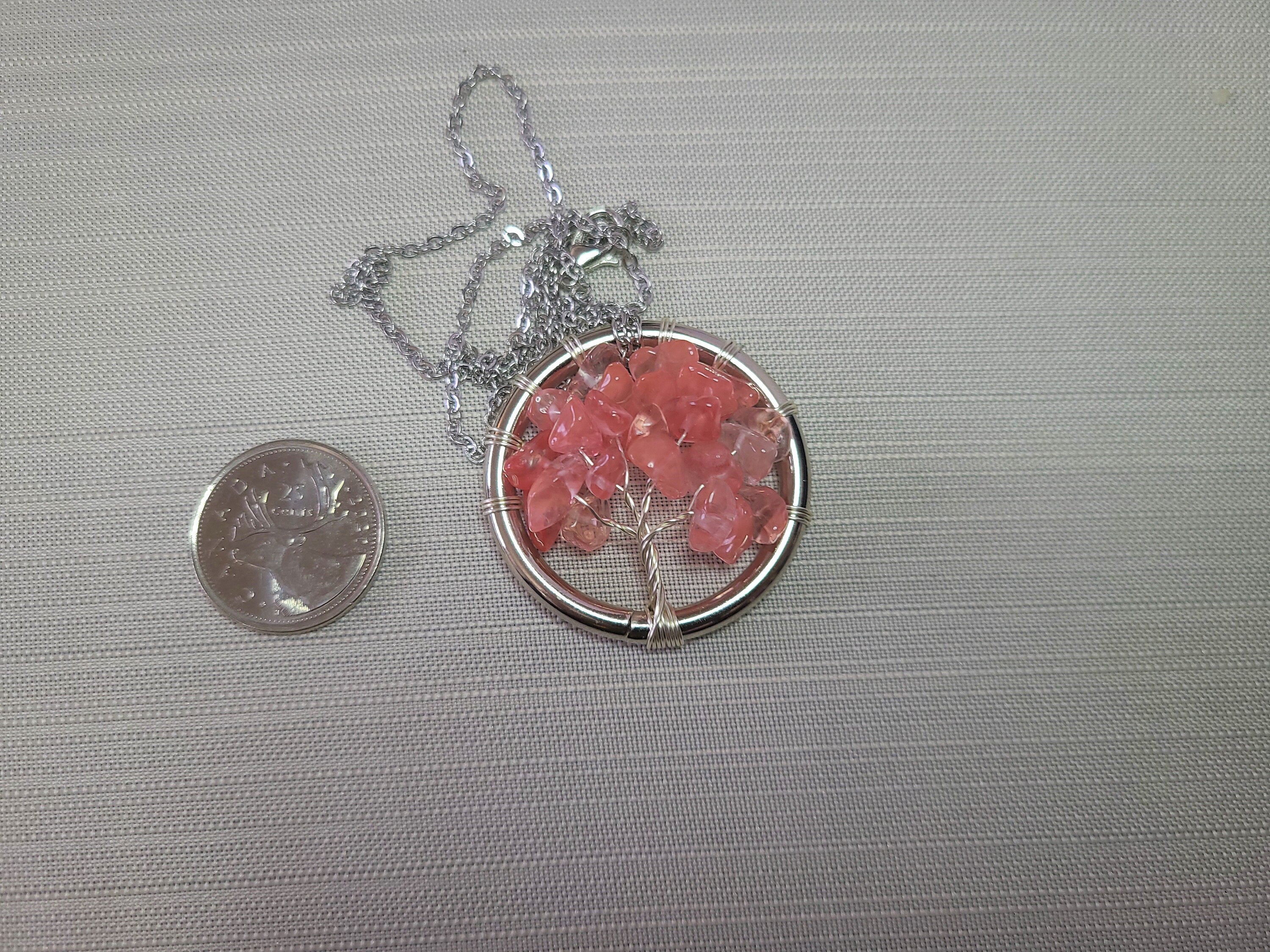 Necklace with pink stone pendant next to a quarter on a gray background