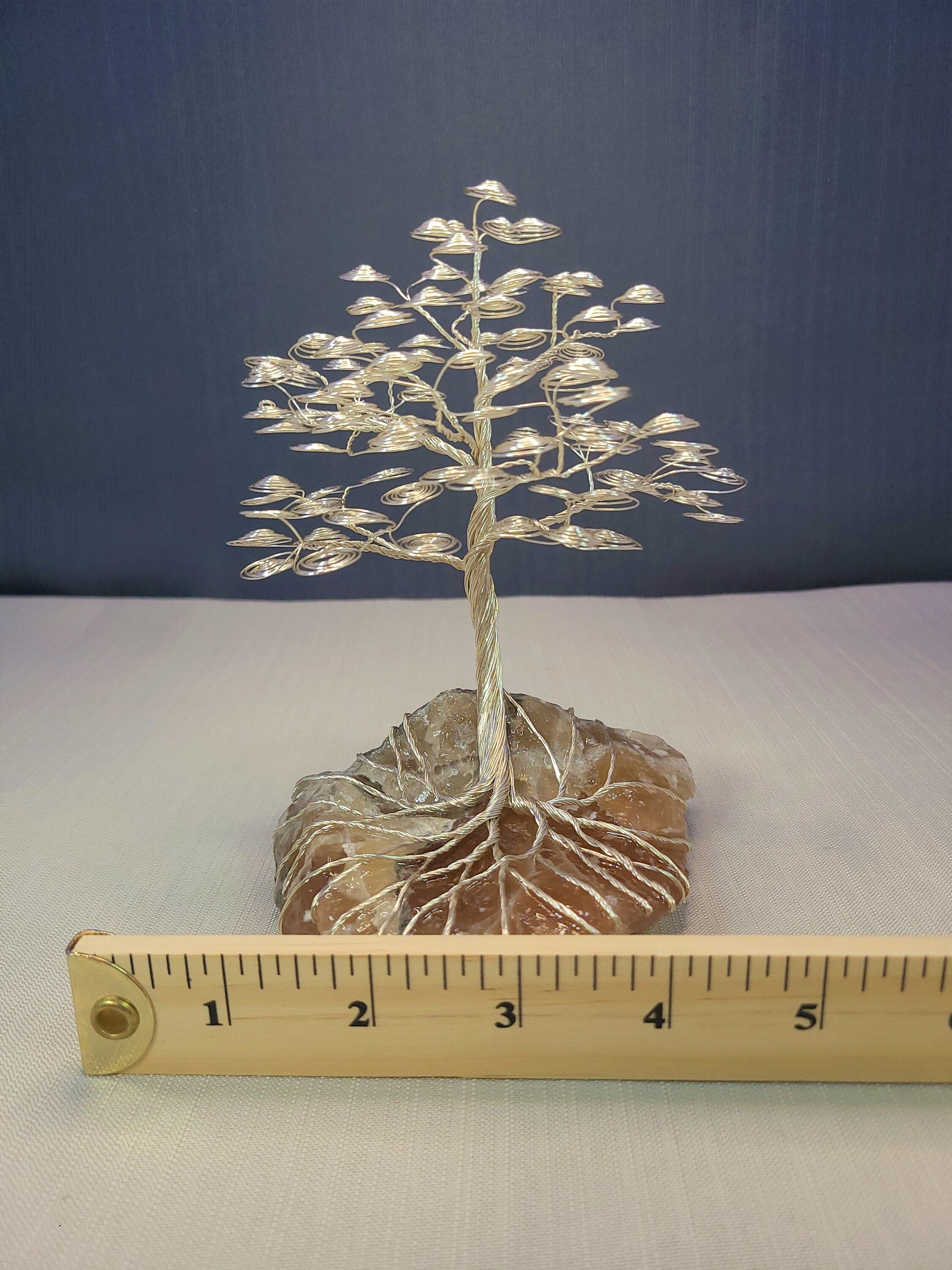Decorative metal tree sculpture on a stone base with a ruler for scale against a blue background