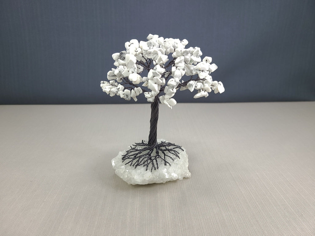 Small tree sculpture with white flowers on a gray surface and dark background