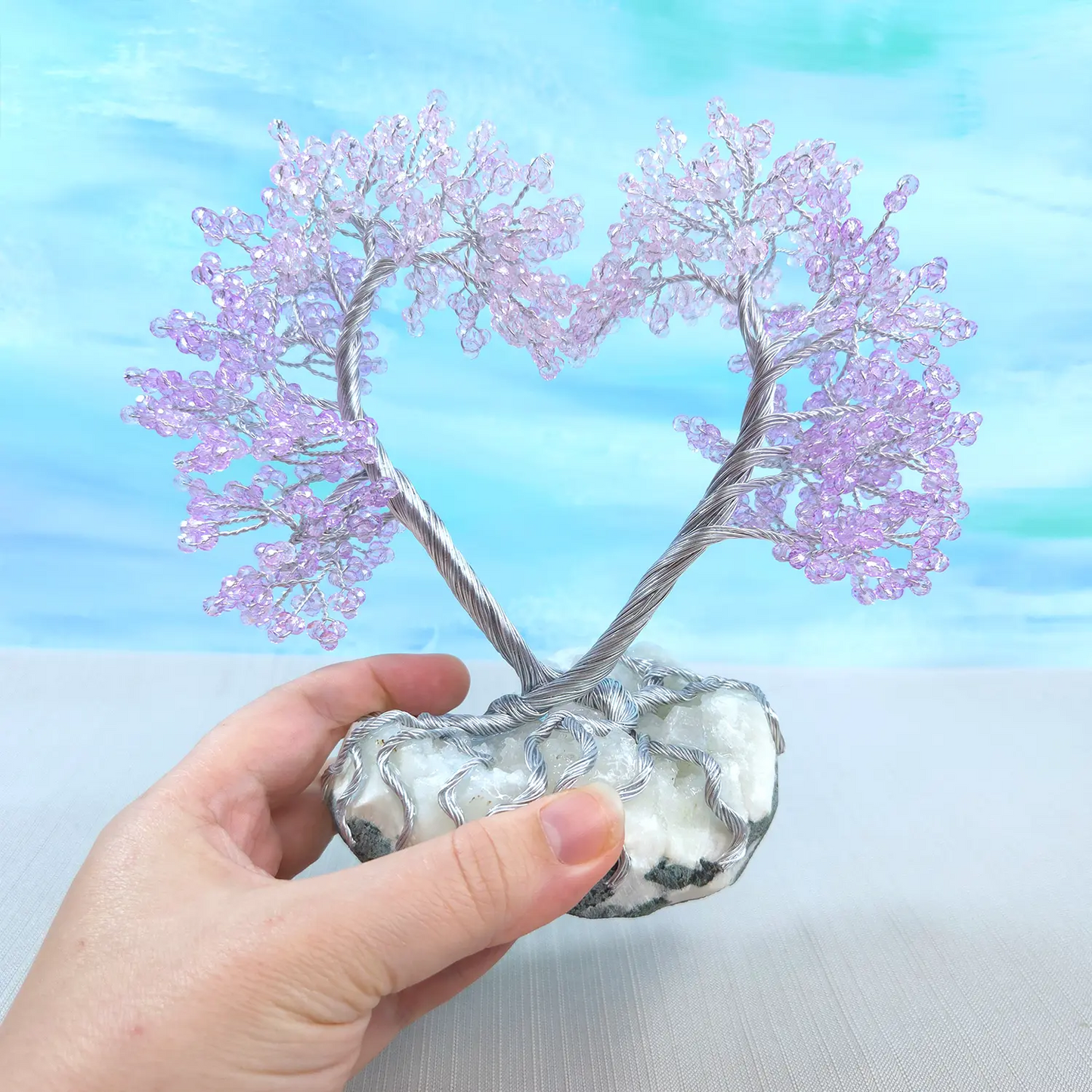 Hand holding a small tree with pink branches on a light blue background