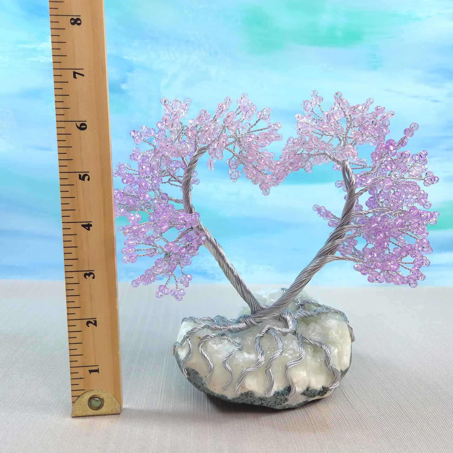 Decorative tree with pink beads on a rock base next to a ruler for scale against a blue sky background.