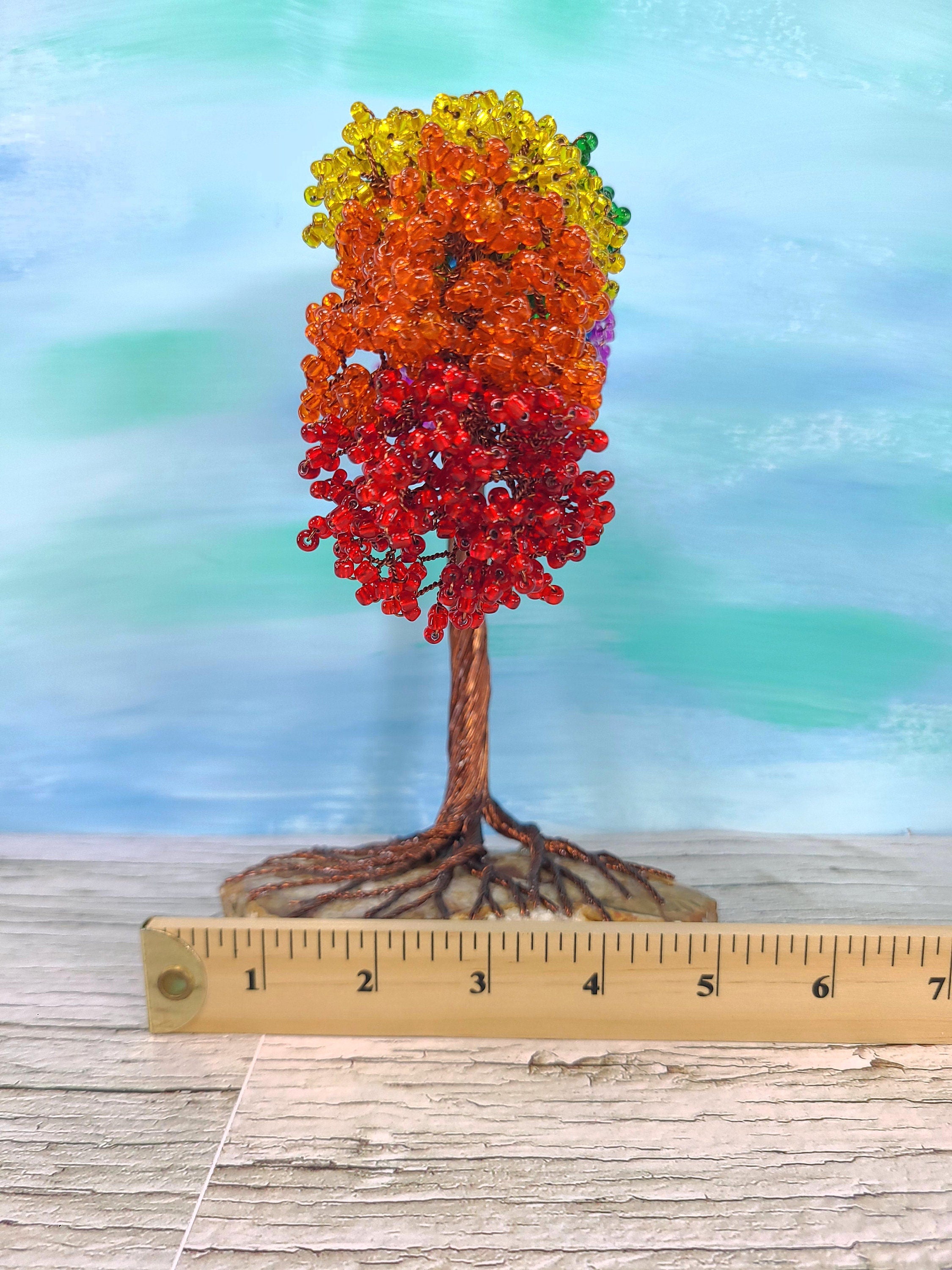 Colorful beaded tree sculpture with a ruler for scale on a wooden surface