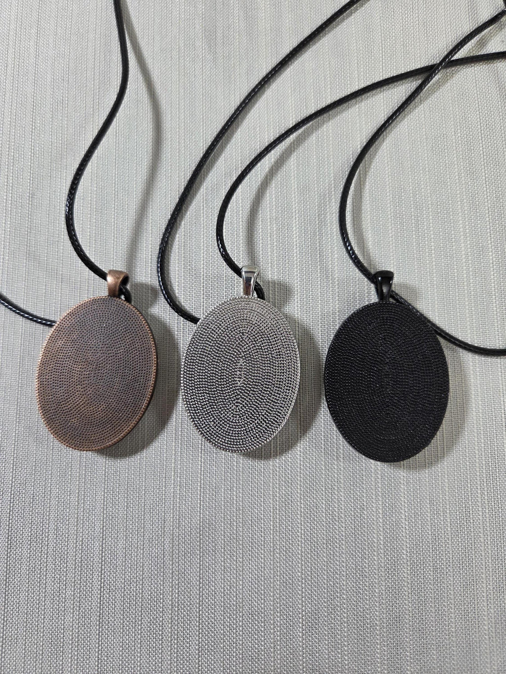 Three oval-shaped pendant necklaces on black cords against a light gray background