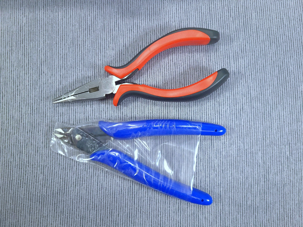 Two pairs of pliers on a textured gray surface