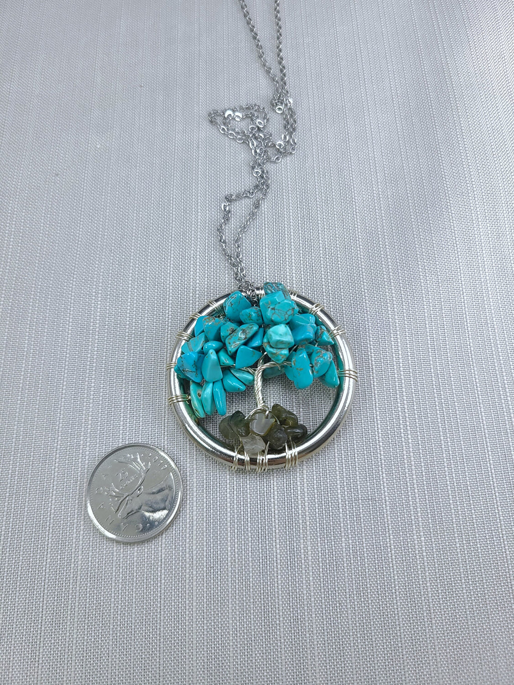 Necklace with turquoise and green stone pendant next to a coin on a gray background