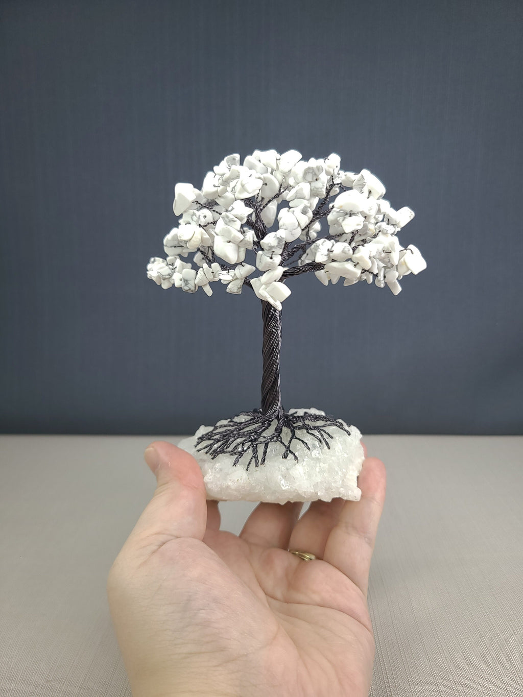 Hand holding a small tree sculpture made of white stones on a gray background