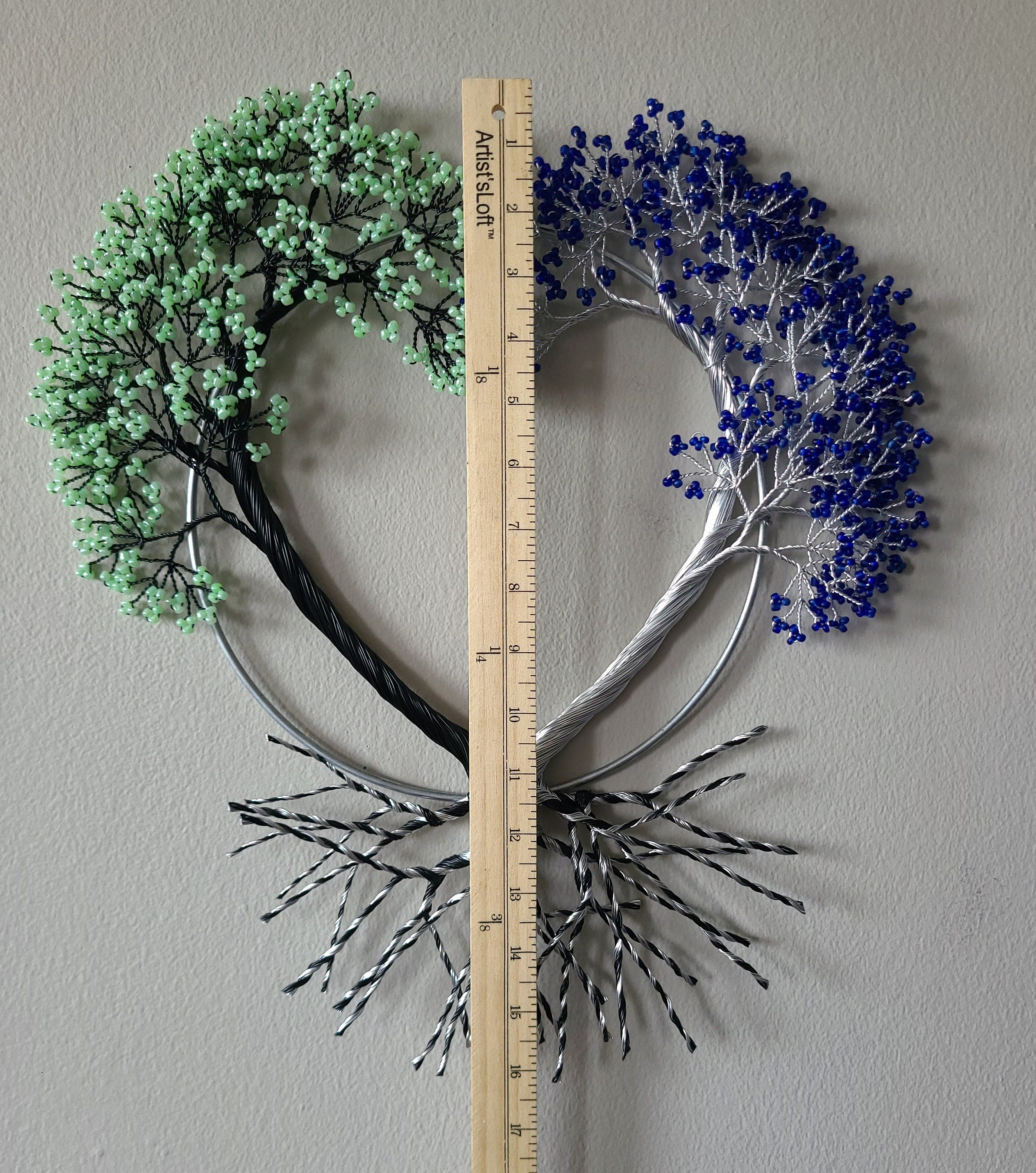 Heart-shaped wall art with green, blue, and silver branches on a gray background