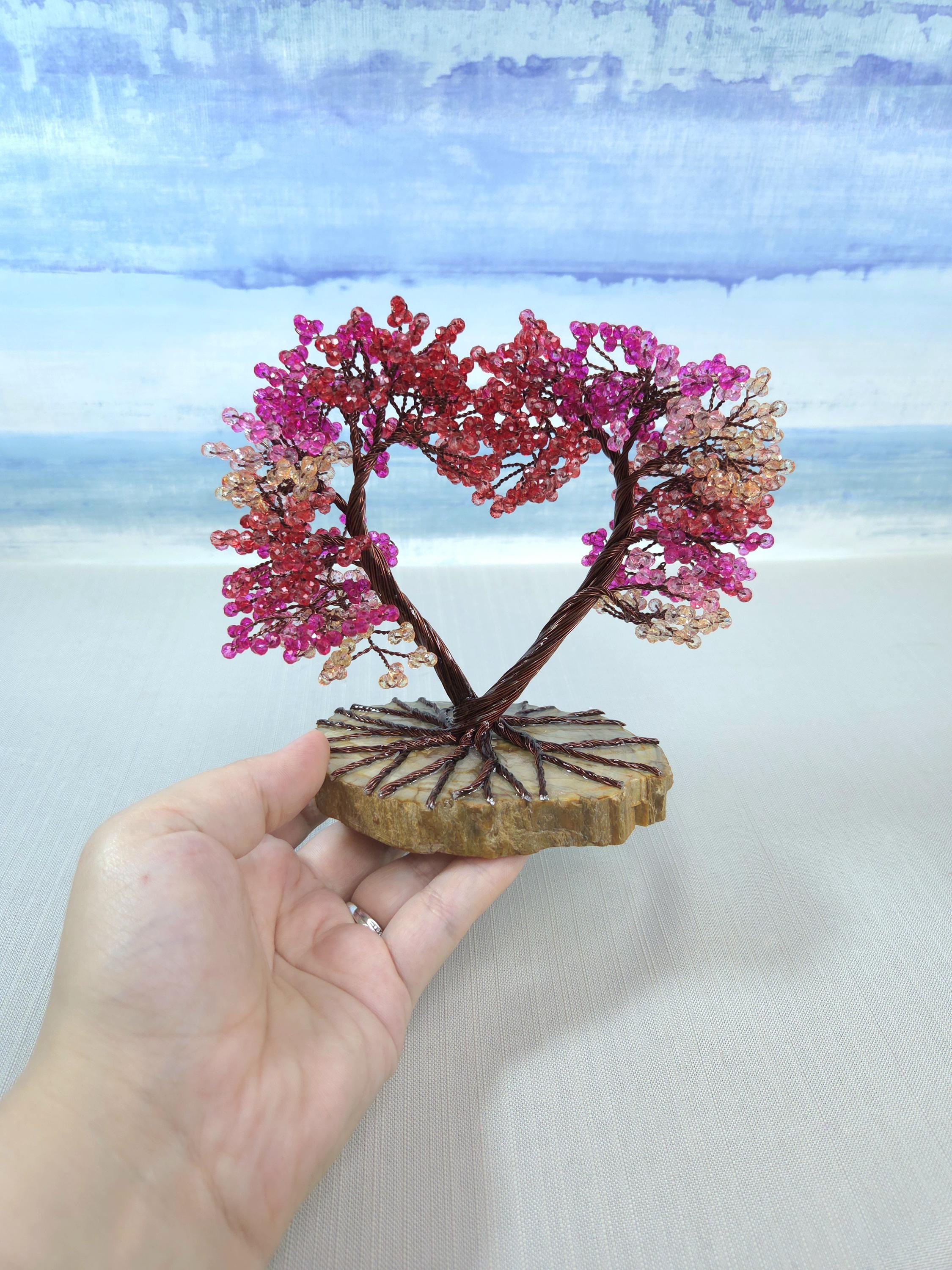 Hand holding a small tree-shaped decorative item with pink and red beads against a light background