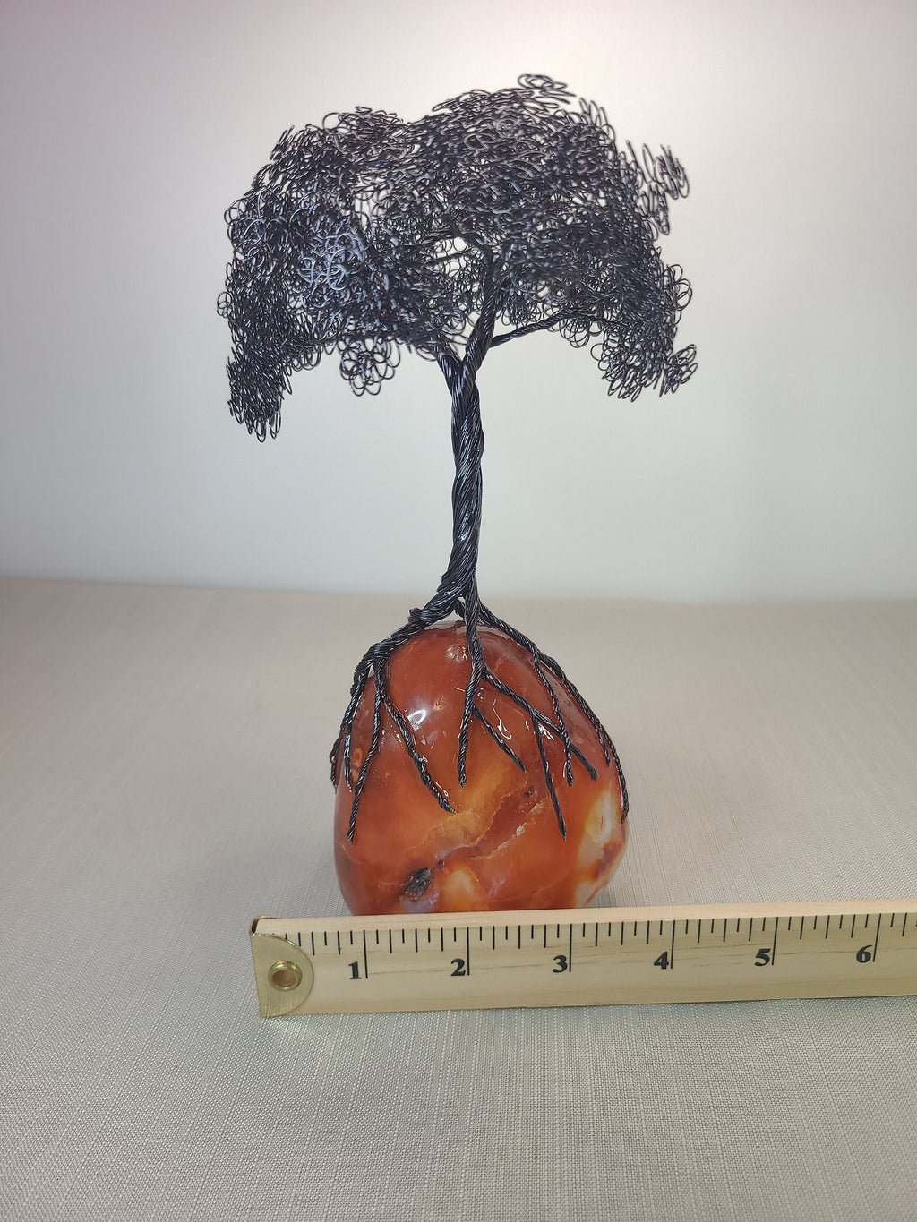 Wire tree sculpture on a stone base with a ruler for scale.