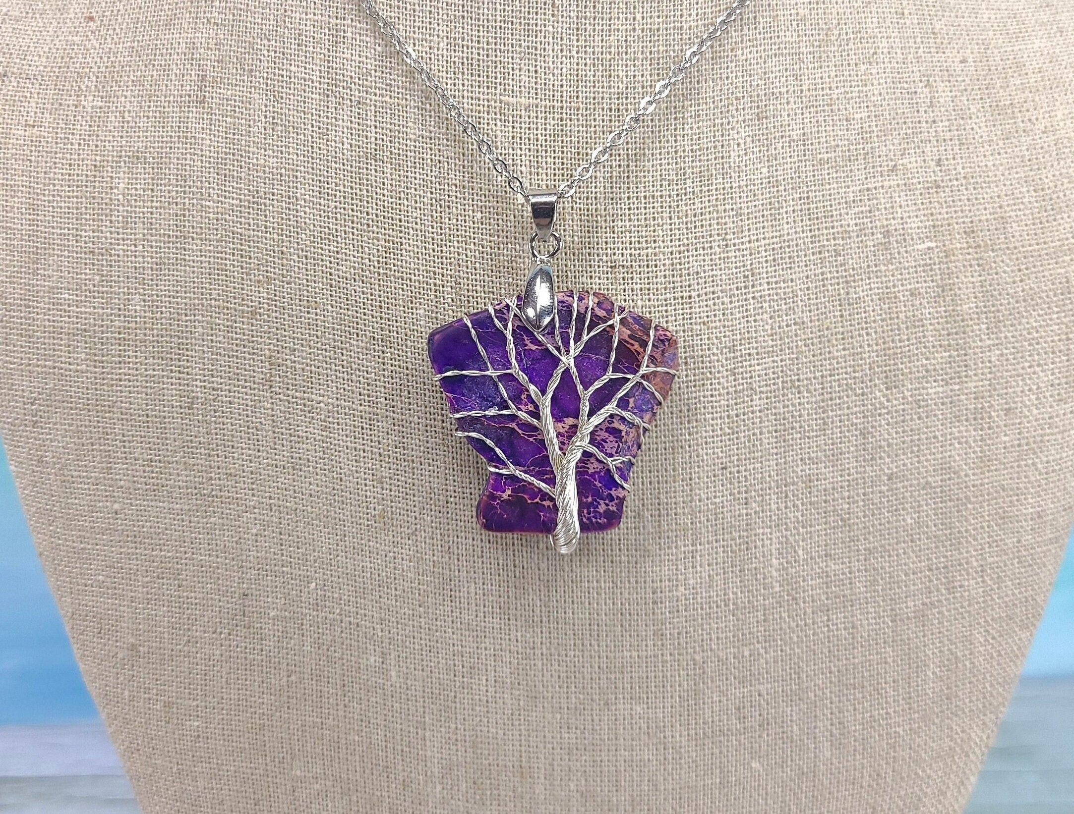 Purple tree-shaped pendant on a silver chain against a beige background