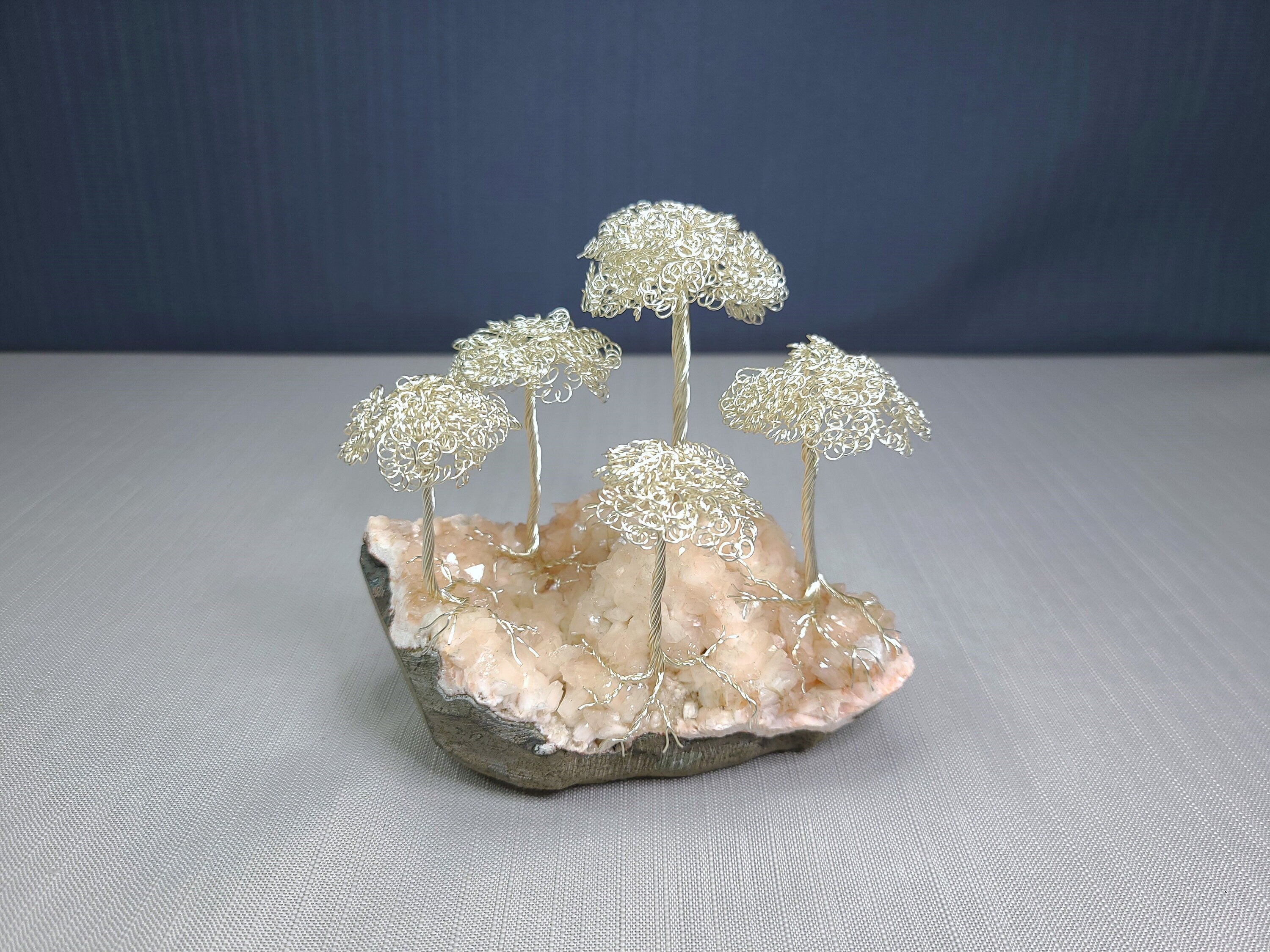 Decorative sculpture of wire trees on a rock base with a blue background