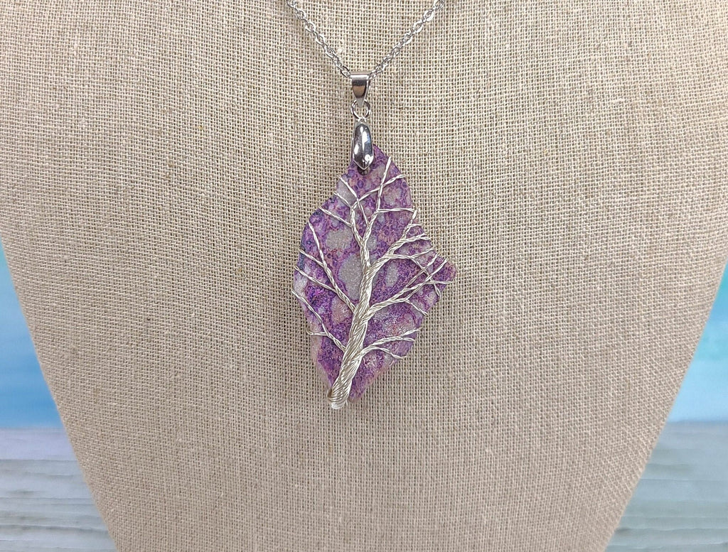 Purple leaf-shaped pendant on a silver chain against a beige fabric background