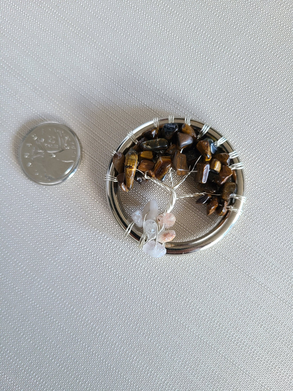 Small round container filled with decorative stones next to a coin on a light gray background