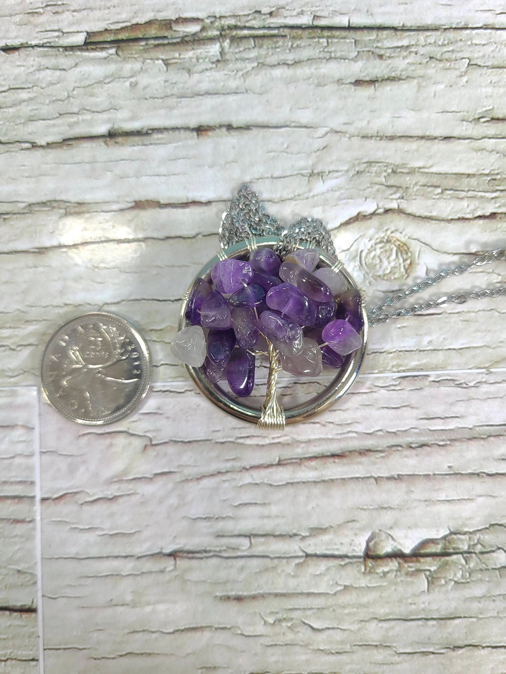 Amethyst tree pendant on a wooden surface with a coin for scale
