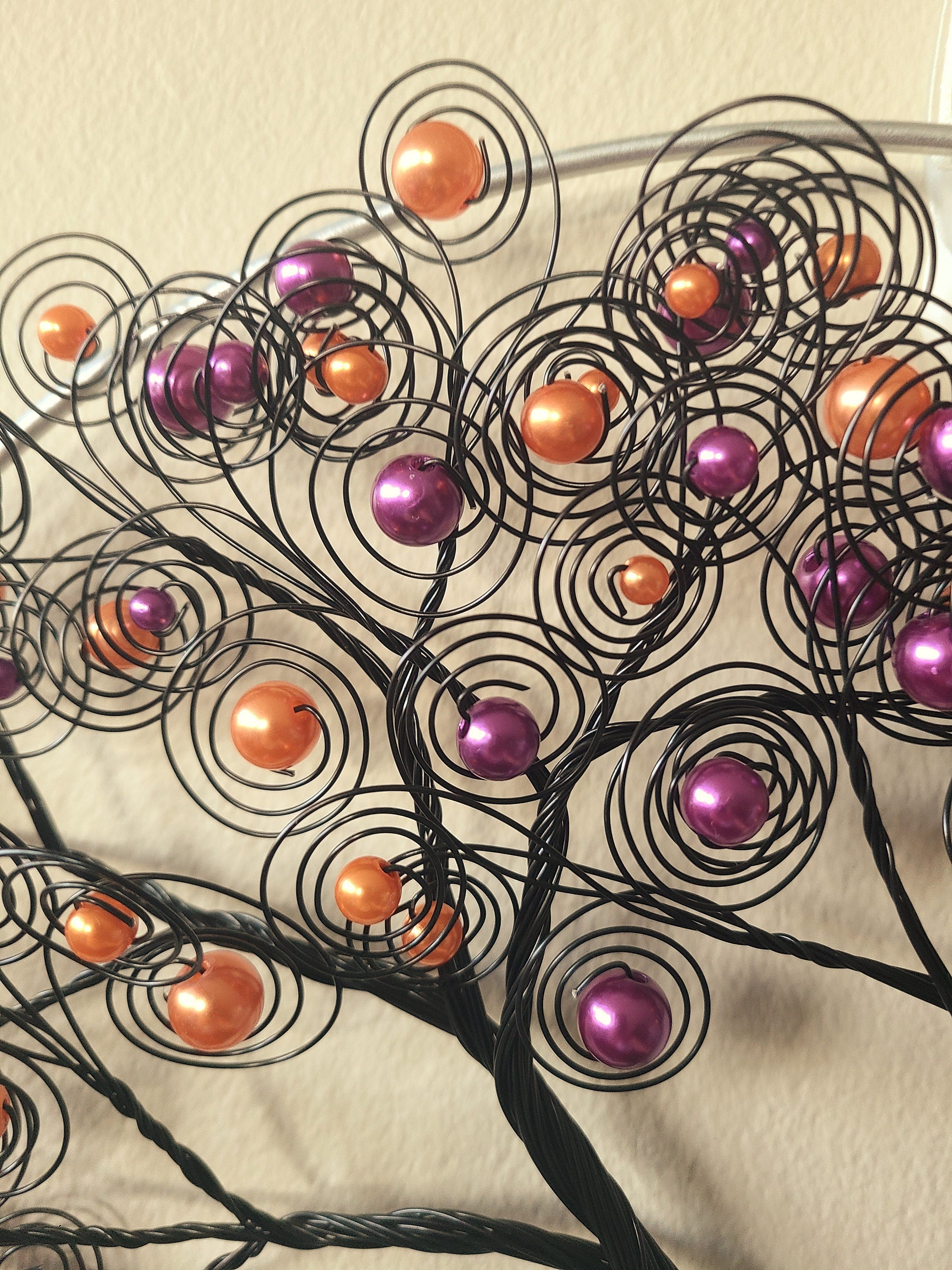 Decorative wall art with black wire branches and colorful beads on a beige background
