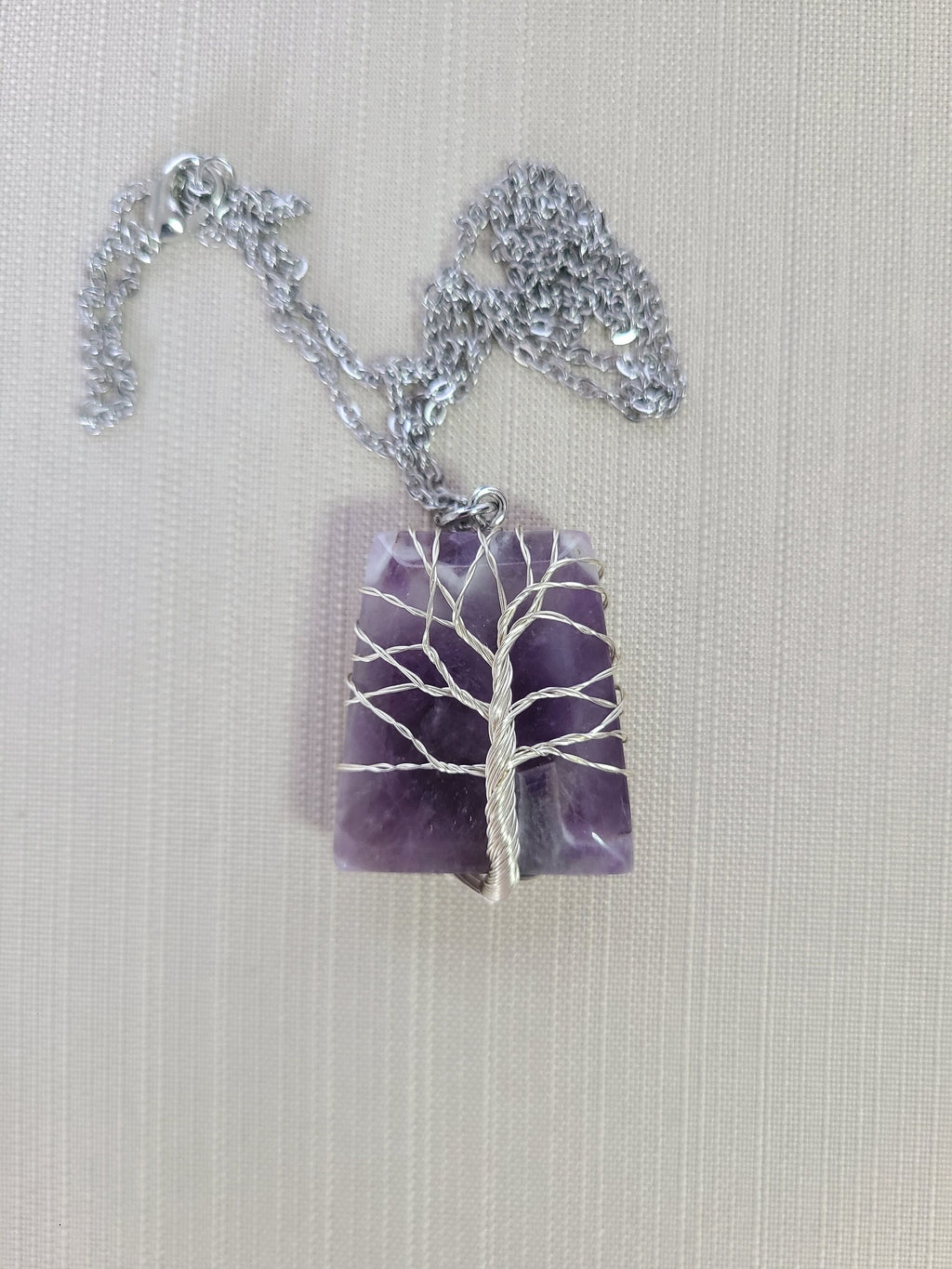 Necklace with a purple amethyst pendant featuring a silver tree design on a light background